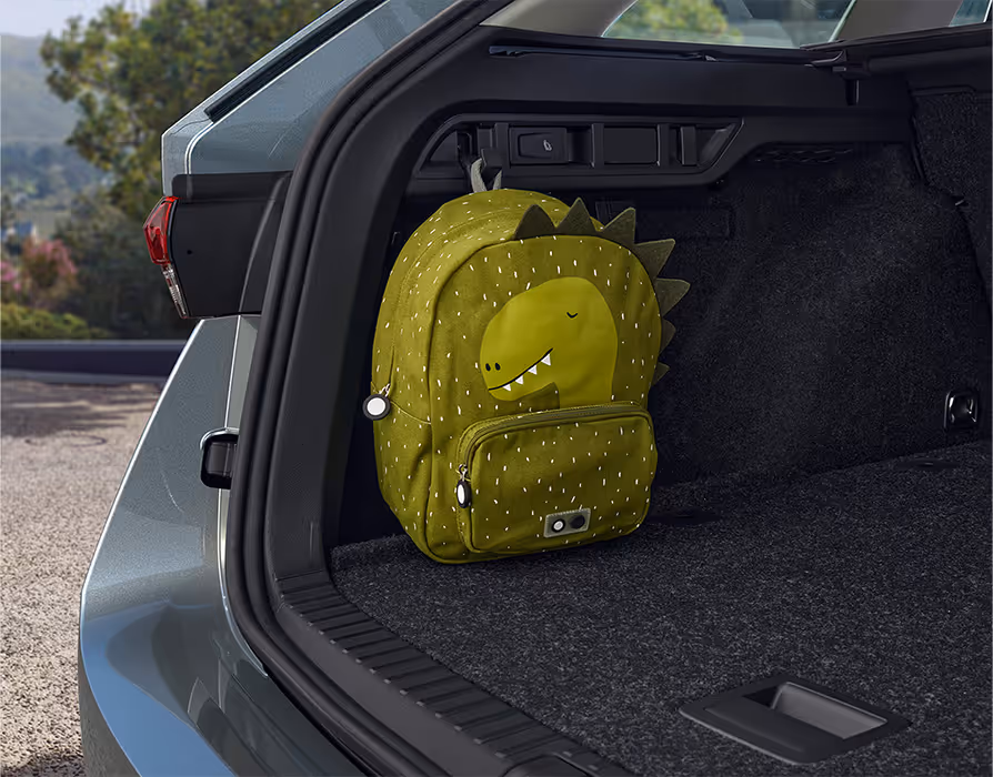 Eine Nahaufnahme des geöffneten Kofferraums eines Škoda Octavia Combi zeigt einen grünen Kinderrucksack mit Dinosaurier-Motiv. Der Rucksack hängt an einem der robusten Haken an der Seitenwand des Laderaums.