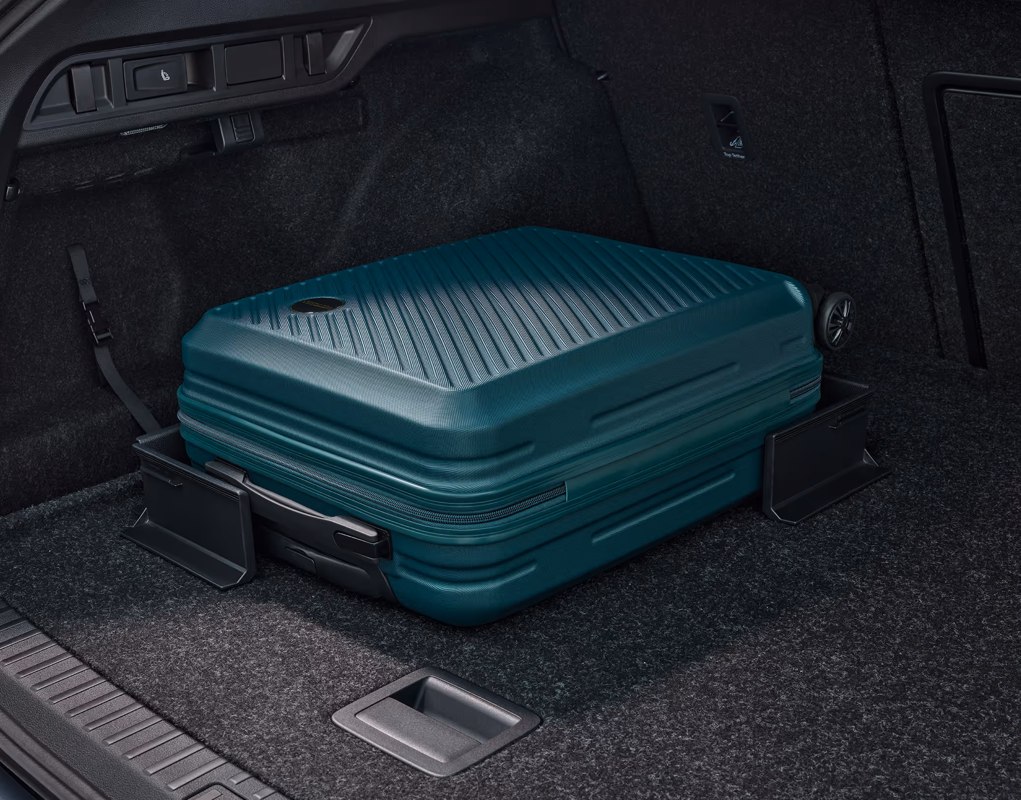 Eine Nahaufnahme des geöffneten Kofferraums eines Škoda Octavia Combi zeigt einen grünen Hartschalenkoffer, der durch zwei schwarze Cargo-Elemente gesichert wird. Diese haften mit Klettverschluss am Kofferraumteppich und verhindern so ein Verrutschen der Ladung.