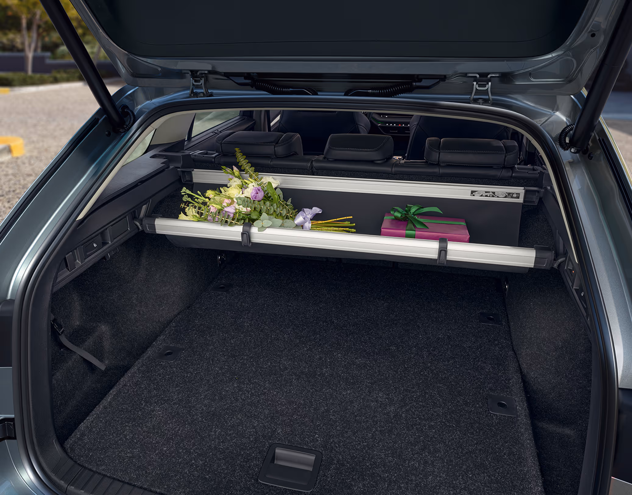 Eine Ansicht des geöffneten Kofferraums eines Škoda Octavia Combi zeigt die multifunktionale Ablagetasche unter der Gepäckraumabdeckung. In dieser werden ein Blumenstrauß und ein verpacktes Geschenk aufbewahrt.