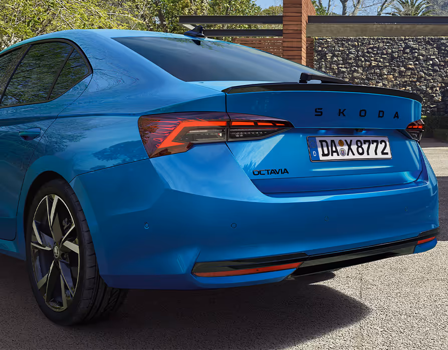 Schräge Heckansicht des Škoda Elroq Sportline in der Farbe Race-Blau Metallic vor grünem Studiohintergrund. Die schwarzen Akzente, wie der Dachkantenspoiler und der Schriftzug, heben das sportliche Design hervor.