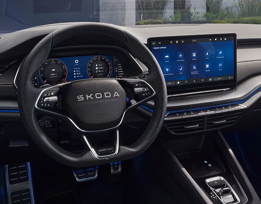 Eine Ansicht aus der Fahrerperspektive zeigt das Cockpit eines Škoda Octavia Sportline. Das sportliche Interieur ist mit einem perforierten Sport-Multifunktionslenkrad mit Sportline-Plakette, einer Pedalerie in Edelstahloptik sowie einer blauen Ambientebeleuchtung ausgestattet. Das digitale Cockpit und das Infotainment-Display zeigen verschiedene Fahr- und Fahrzeugeinstellungen.