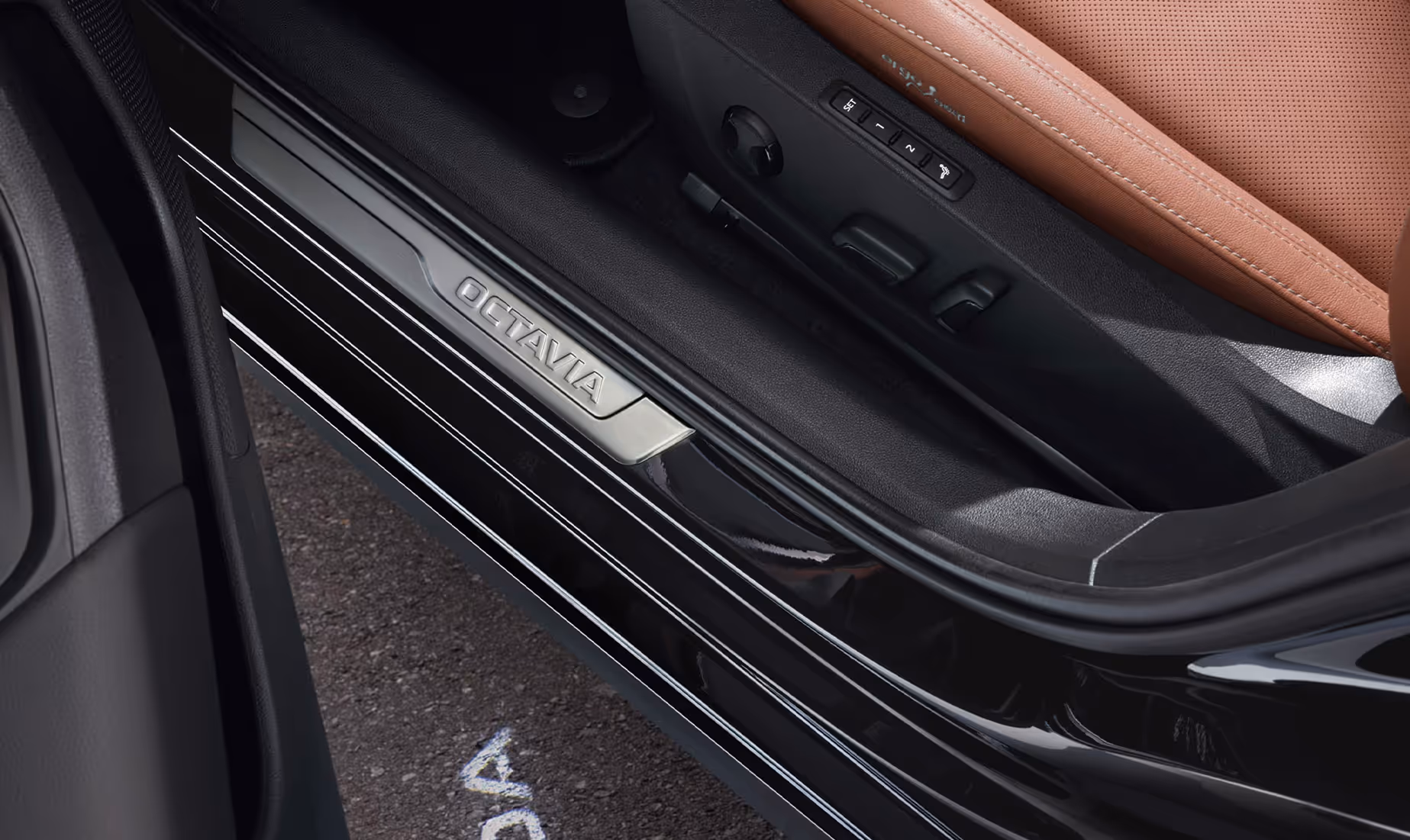 Eine Aufnahme aus der Vogelperspektive zeigt den geöffneten Türbereich eines Škoda Octavia. Auf den dunklen Asphalt wird der „ŠKODA“ Schriftzug des Welcome-Logos projiziert. Im Türschweller ist eine Dekorleiste mit dem Schriftzug „OCTAVIA“ zu sehen, und an der Seite des cognac-farbenen Ledersitzes befinden sich die Bedienelemente für die elektrische Sitzverstellung.