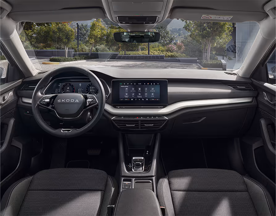 Blick über die Mittelarmlehne auf das Lenkrad, das Infotainmentsystem und das Armaturenbrett im Škoda Elroq in der Ausstattungslinie “Loft”.