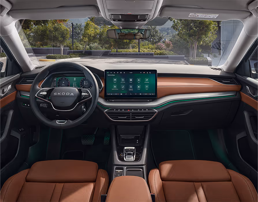 Blick über die Mittelarmlehne auf das Lenkrad, das Infotainmentsystem und das Armaturenbrett im Škoda Elroq. Türkise Ambient-Beleuchtung.