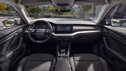 Eine weite Innenansicht zeigt das gesamte Cockpit eines Škoda Octavia mit der Design Selection Loft. Das Interieur ist mit einer Stoff-Microfaser-Kombination in Grau/Schwarz und einer Dekorleiste in gebürsteter Aluminium-Optik am Armaturenbrett ausgestattet. Durch die Windschutzscheibe ist eine begrünte, städtische Umgebung zu sehen.