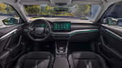 Eine weite Innenansicht zeigt das gesamte Cockpit eines Škoda Octavia mit der Design Selection Lounge. Das Interieur ist mit einer Microfaser-Stoff-Kunstleder-Kombination in Grau mit hellgrauen Kontrastnähten und einer Dekorleiste in Anodised-Cross-Optik am Armaturenbrett ausgestattet. Durch die Windschutzscheibe ist eine begrünte, städtische Umgebung zu sehen.