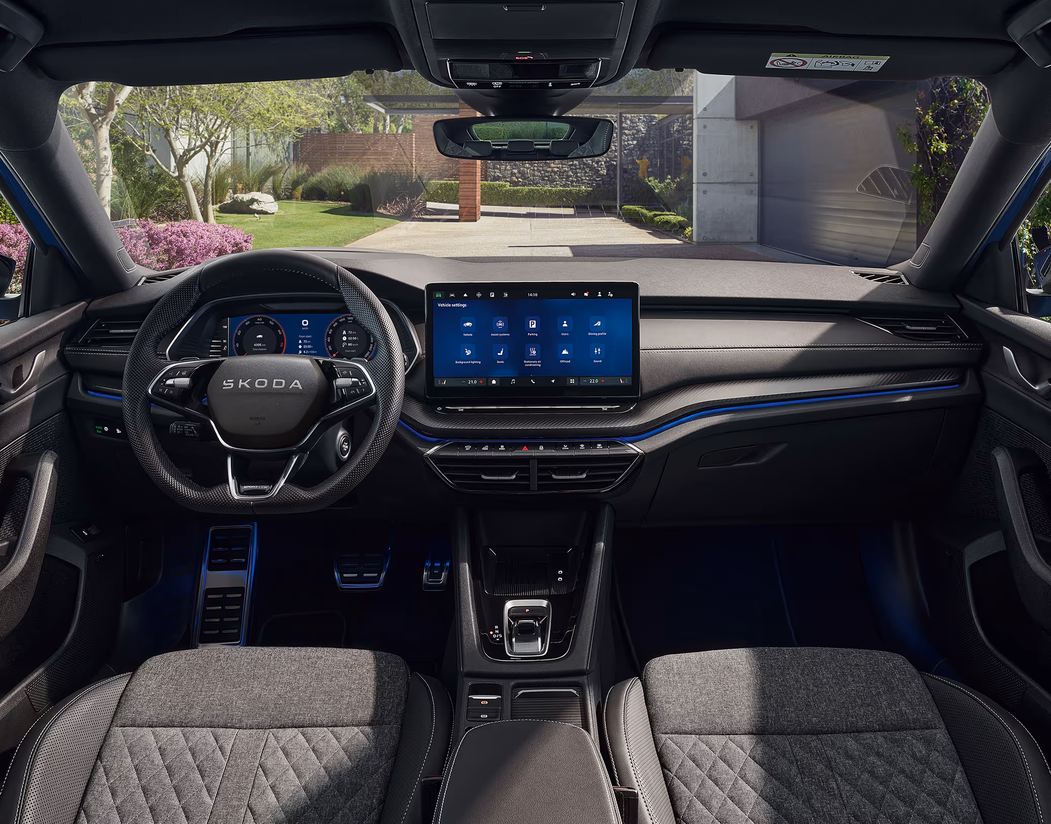 Eine weite Innenansicht zeigt das gesamte Cockpit eines Škoda Octavia mit der Design Selection Sportline. Das sportliche, dunkle Interieur ist mit Sportsitzen aus ThermoFlux-Stoff mit integrierten Kopfstützen und einer Dekorleiste in Carbon-Optik am Armaturenbrett ausgestattet. Durch die Windschutzscheibe ist eine begrünte, städtische Umgebung zu sehen.