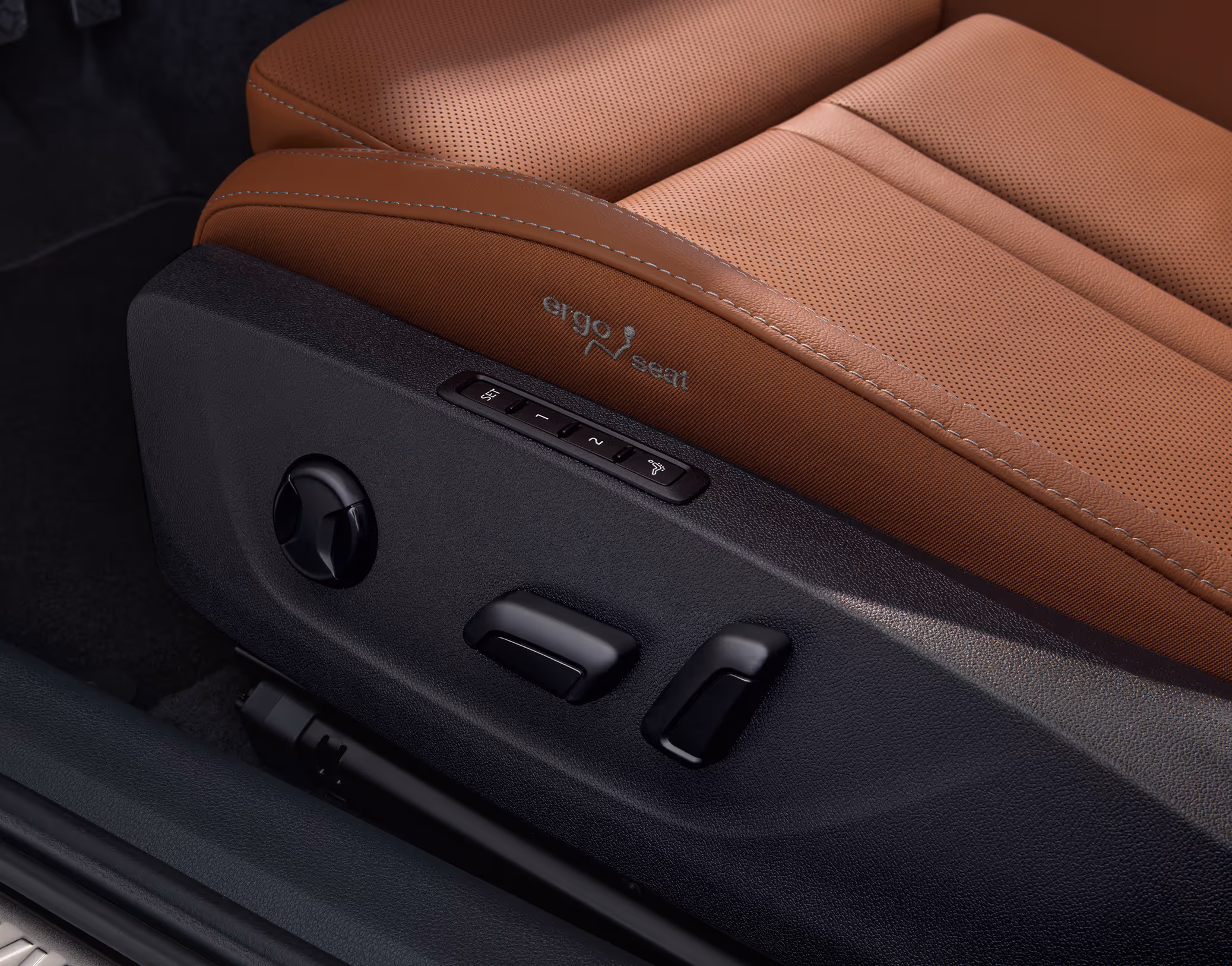 Eine Nahaufnahme zeigt den Ergo-Komfortsitz eines Škoda Octavia, der mit cognac-braunem, perforiertem Leder der Design Selection Suite bezogen ist. An der Seite des Sitzes sind die Bedienelemente für die elektrische Verstellung und die Massagefunktion sowie der eingestickte „ergo seat“-Schriftzug zu sehen.