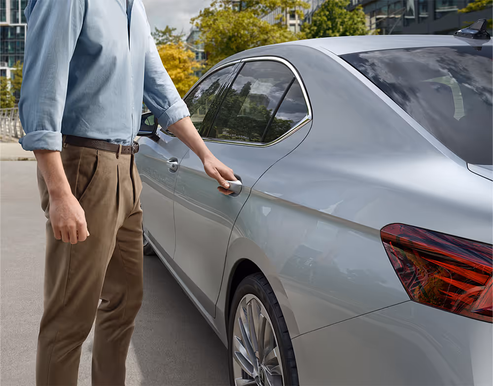Eine Nahaufnahme zeigt einen Mann, der den Türgriff einer Škoda Superb Limousine in der Lackierung Aluminium-Silber Metallic ergreift.