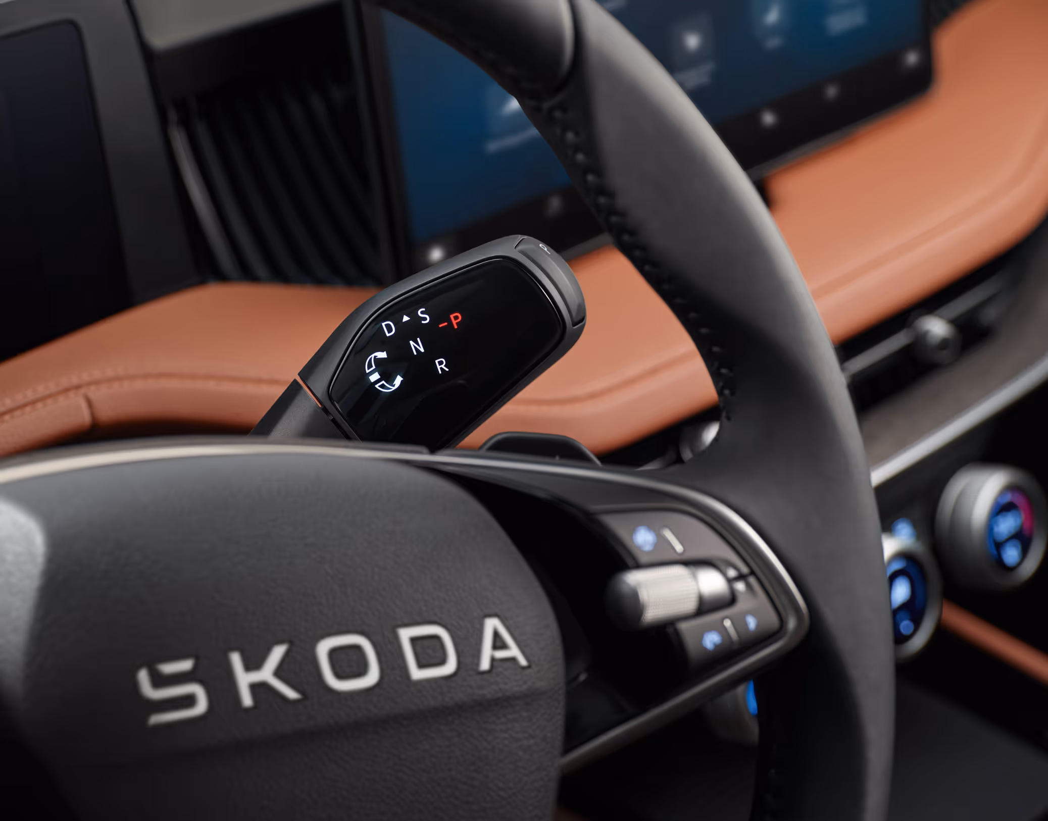 Eine Nahaufnahme des Cockpits eines Škoda Superb zeigt den neuen, an der Lenksäule positionierten Wählhebel für das Automatikgetriebe. Im Vordergrund ist das Multifunktionslenkrad mit dem Škoda Schriftzug zu sehen, während im Hintergrund das cognac-farbene Leder der Design Selection Suite erkennbar ist.