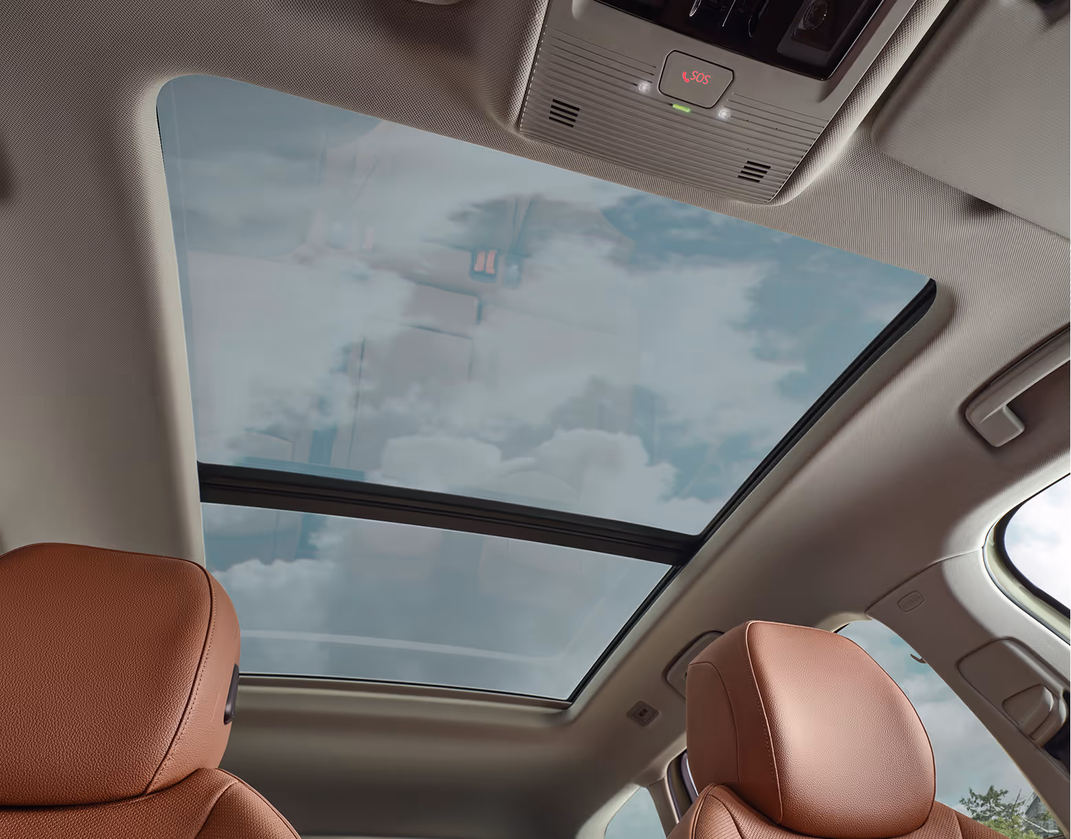 Ein Blick nach oben im Innenraum eines Škoda Superb zeigt das große, optionale Panoramaschiebedach, durch das der leicht bewölkte Himmel zu sehen ist. Die Aufnahme zeigt auch die Kopfstützen der cognac-farbenen Ledersitze und die Dachkonsole mit dem roten SOS-Knopf für den Notruf.