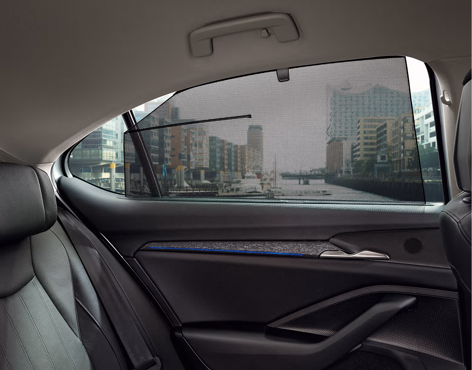 Ein Bild zeigt das mechanische Sonnenschutzrollo, das am hinteren Seitenfenster eines Škoda Superb hochgezogen ist. Die Türverkleidung der Design Selection Suite ist mit einer Dekorleiste in Unique Dark Chrome und blauer Ambientebeleuchtung versehen. Durch das Rollo ist eine städtische Hafenszene sichtbar.