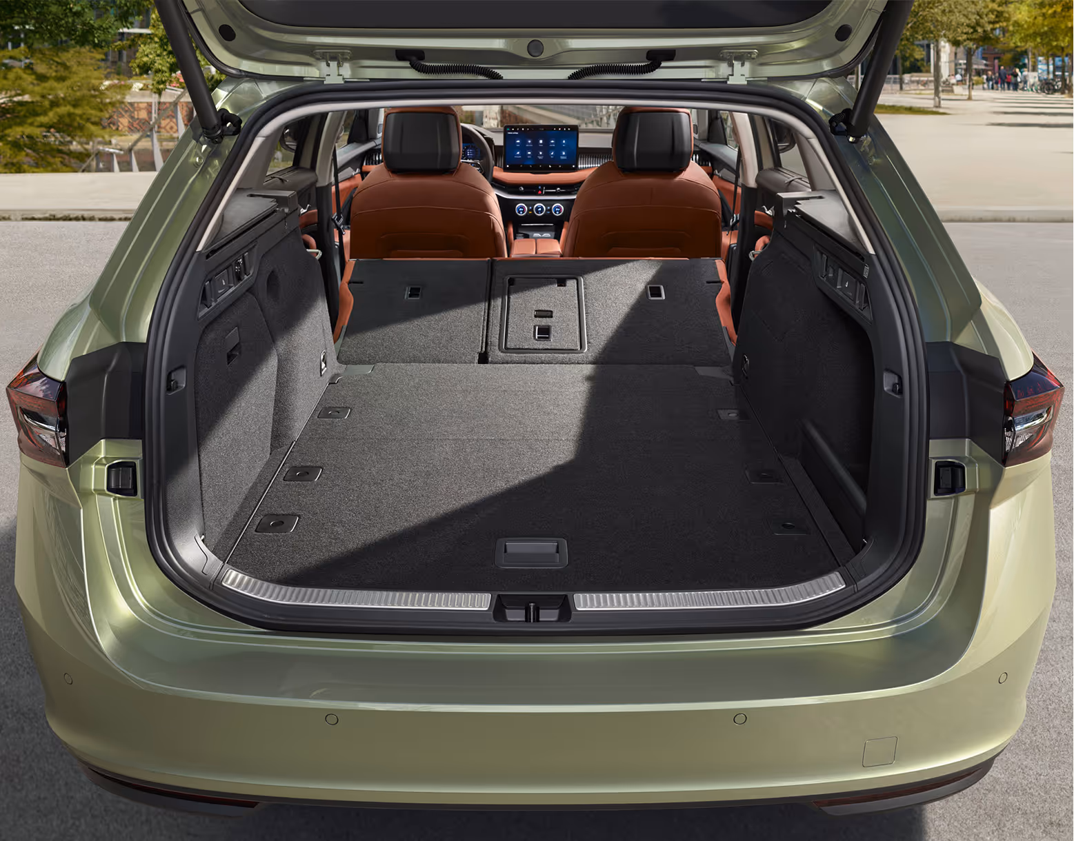 Eine Ansicht des geöffneten Kofferraums eines Škoda Superb Combi zeigt die maximale Ladekapazität. Die Rücksitzlehnen sind umgeklappt und schaffen eine durchgehend ebene Ladefläche, die den Blick auf das Cockpit mit den cognac-farbenen Vordersitzen freigibt.