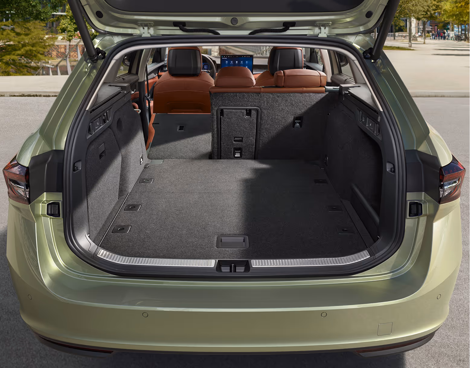 Eine Ansicht des geöffneten Kofferraums eines Škoda Superb Combi zeigt die teilweise umgeklappten Rücksitzlehnen. Dies vergrößert die ebene Ladefläche und gibt den Blick auf das Cockpit mit den cognac-farbenen Vordersitzen frei.