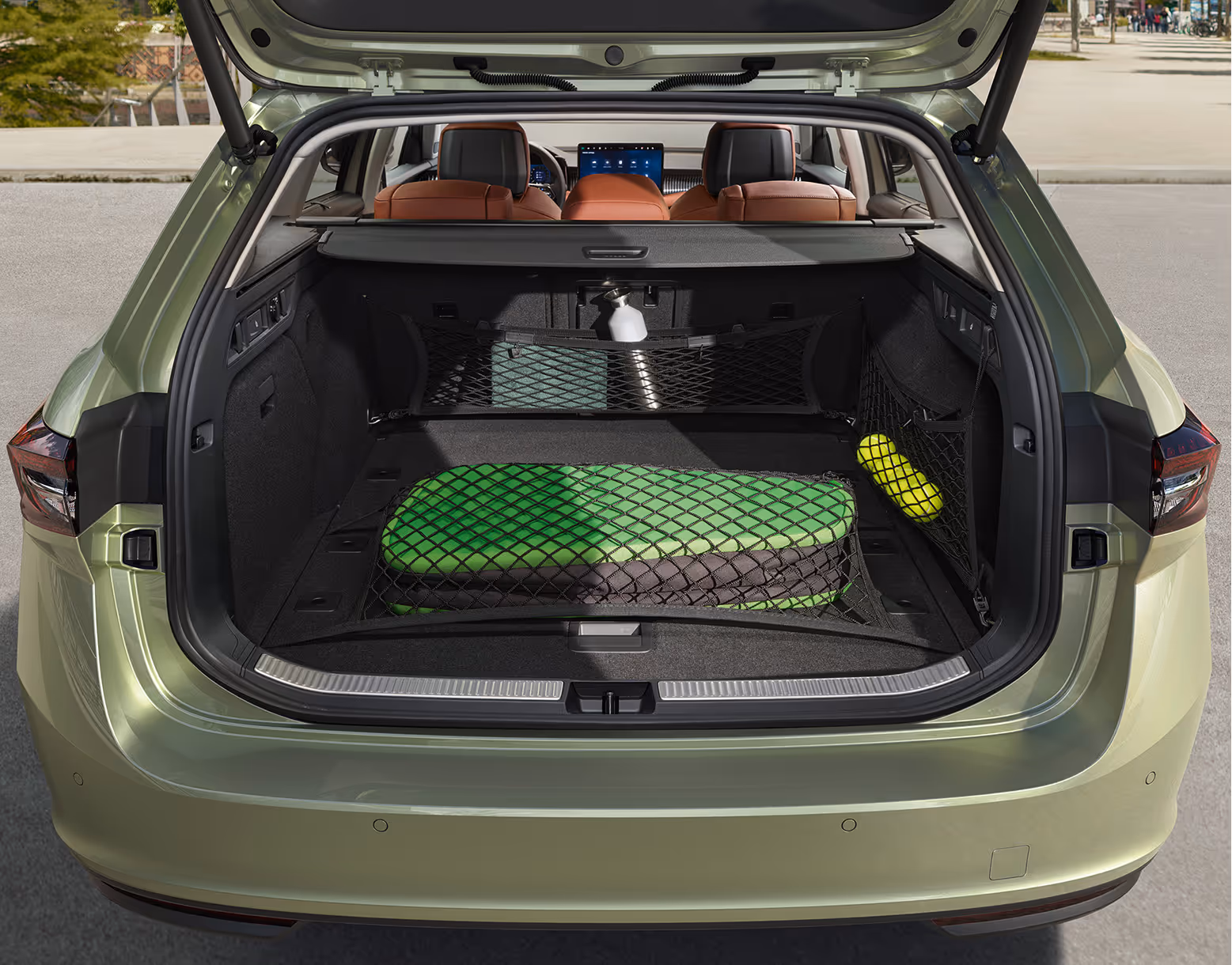 Eine Ansicht des geöffneten Kofferraums eines Škoda Superb Combi zeigt die Anwendung des Netzprogramms. Ein großes Bodennetz sichert eine gefaltete grüne Matte, während weitere Netze an der Seite und hinter den Rücksitzen kleinere Gegenstände wie eine Flasche und Tennisbälle halten.