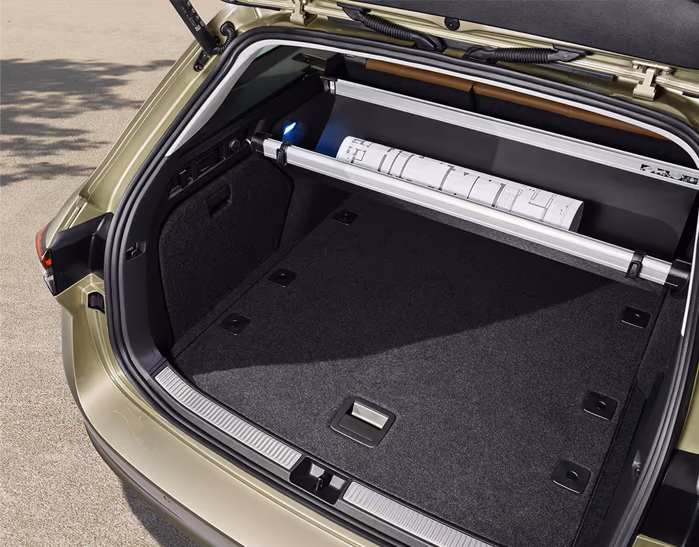 Eine Ansicht des geöffneten Kofferraums eines Škoda Superb Combi zeigt die automatisch abrollende Gepäckraumabdeckung. Die Abdeckung ist halb eingefahren und gibt den Blick auf eine gerollte Bauzeichnung frei, die dahinter aufbewahrt wird.