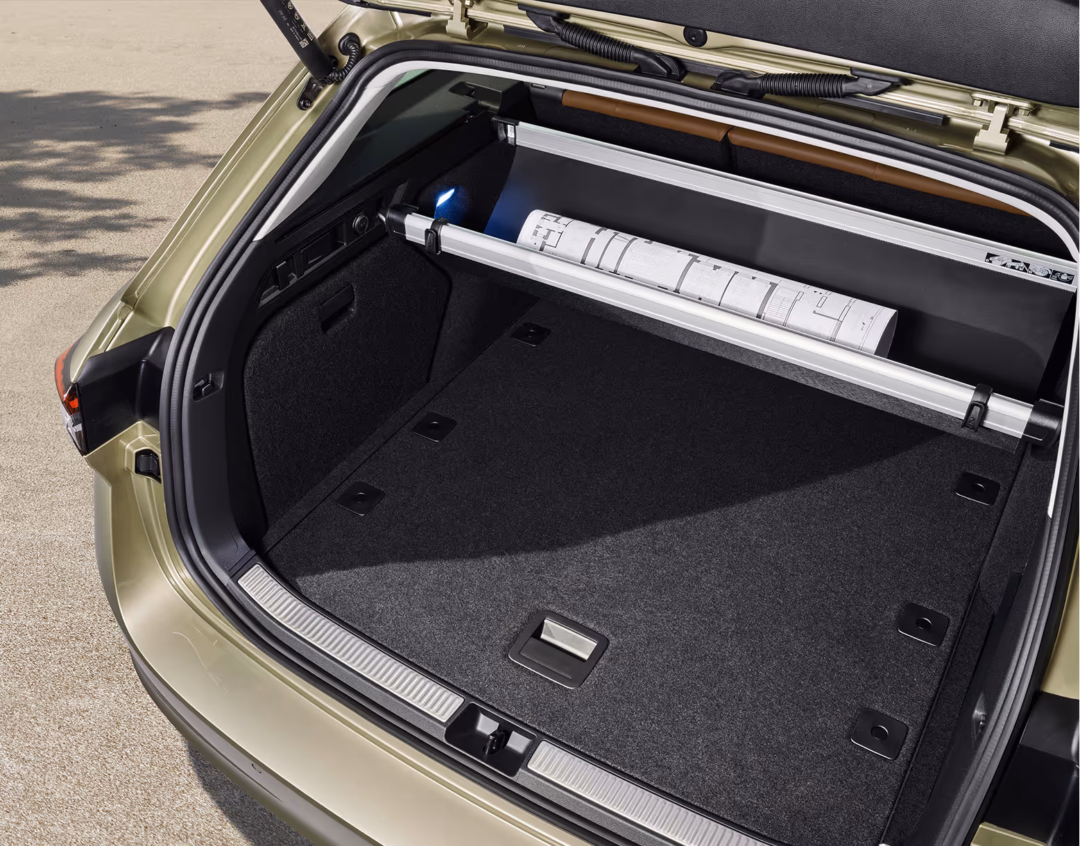 Eine Ansicht des geöffneten Kofferraums eines Škoda Superb Combi zeigt die automatisch abrollende Gepäckraumabdeckung. Die Abdeckung ist halb eingefahren und gibt den Blick auf eine gerollte Bauzeichnung frei, die dahinter aufbewahrt wird.