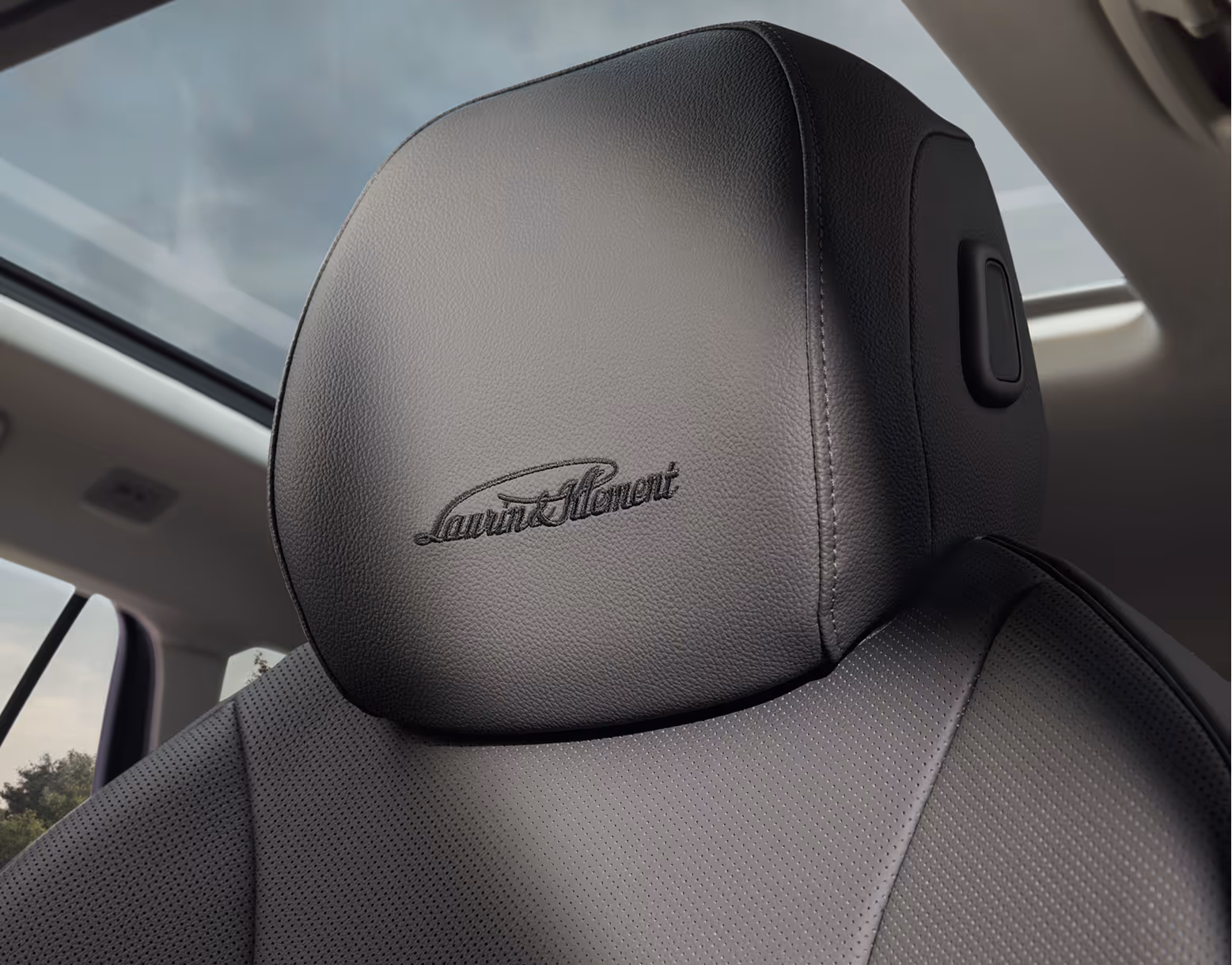 Eine Nahaufnahme zeigt die Kopfstütze eines Vordersitzes im Škoda Superb mit der Design Selection L&K Suite. In den schwarzen, perforierten Ledersitz ist der „Laurin & Klement“-Schriftzug eingestickt, während über dem Sitz das Panoramaschiebedach zu sehen ist.