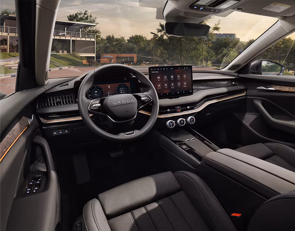 Eine Ansicht aus der Fahrerperspektive zeigt das Cockpit eines Škoda Superb mit der Design Selection L&K Suite in Schwarz. Das Interieur ist mit einem Multifunktionslenkrad mit „Laurin & Klement“-Plakette und Dekorleisten in Unique Dark Chrome ausgestattet. Das digitale Cockpit und der Infotainment-Bildschirm zeigen verschiedene Fahr- und Fahrzeugeinstellungen.