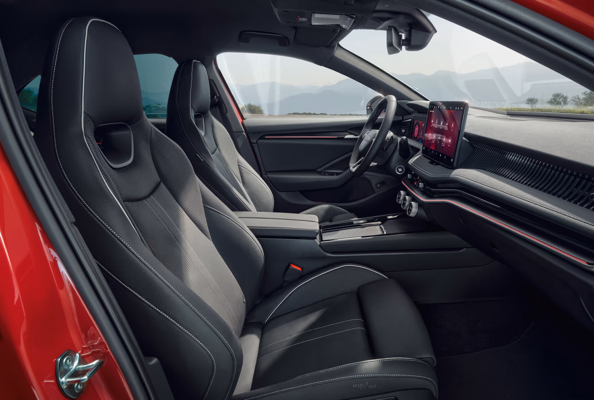 Eine seitliche Innenansicht des Škoda Superb Sportline zeigt das sportliche Interieur der Design Selection Sportline. Die schwarzen Sportsitze mit integrierten Kopfstützen und grauen Kontrastnähten sowie die Dekorleisten in Carbon-Optik prägen das Cockpit. Durch die Fenster ist eine hügelige Landschaft zu sehen.