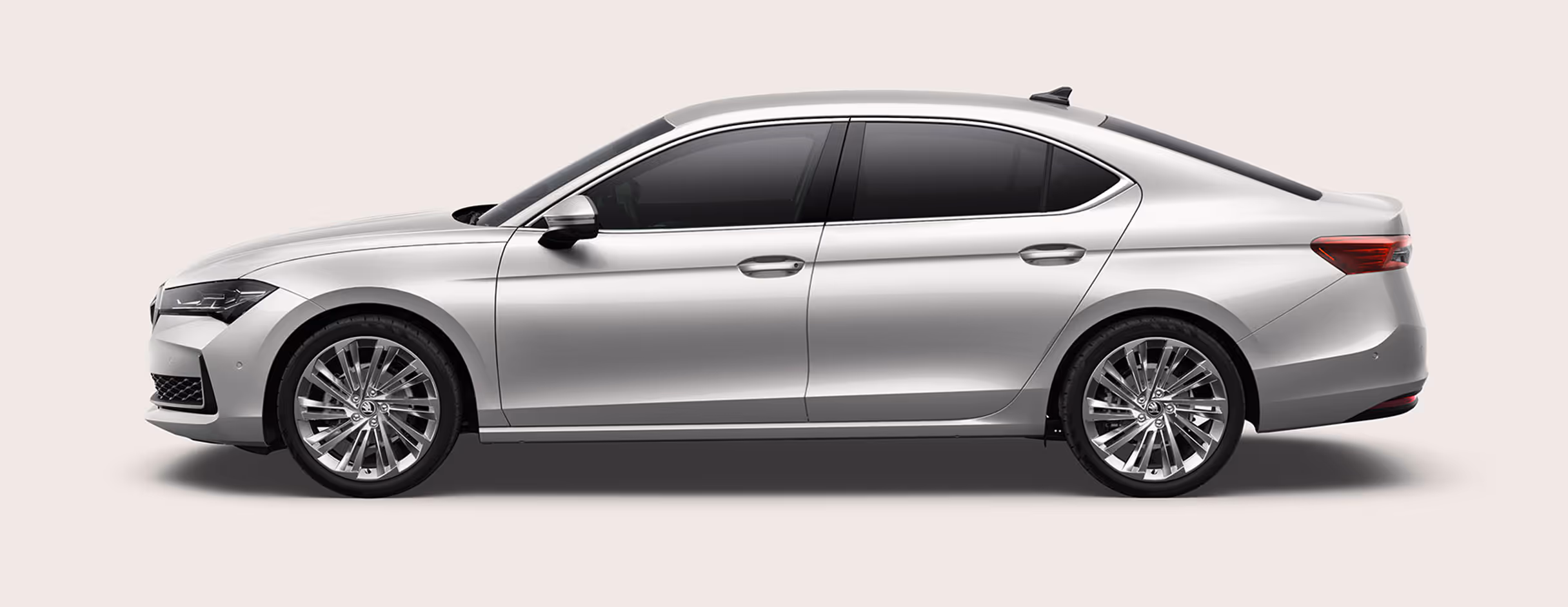 Seitenansicht einer Škoda Superb Limousine in der Lackierung Kristall-Weiß Uni mit 19 Zoll Leichtmetallfelgen “Veritate” vor einem einfarbigen Hintergrund in der Farbe der Fahrzeuglackierung.