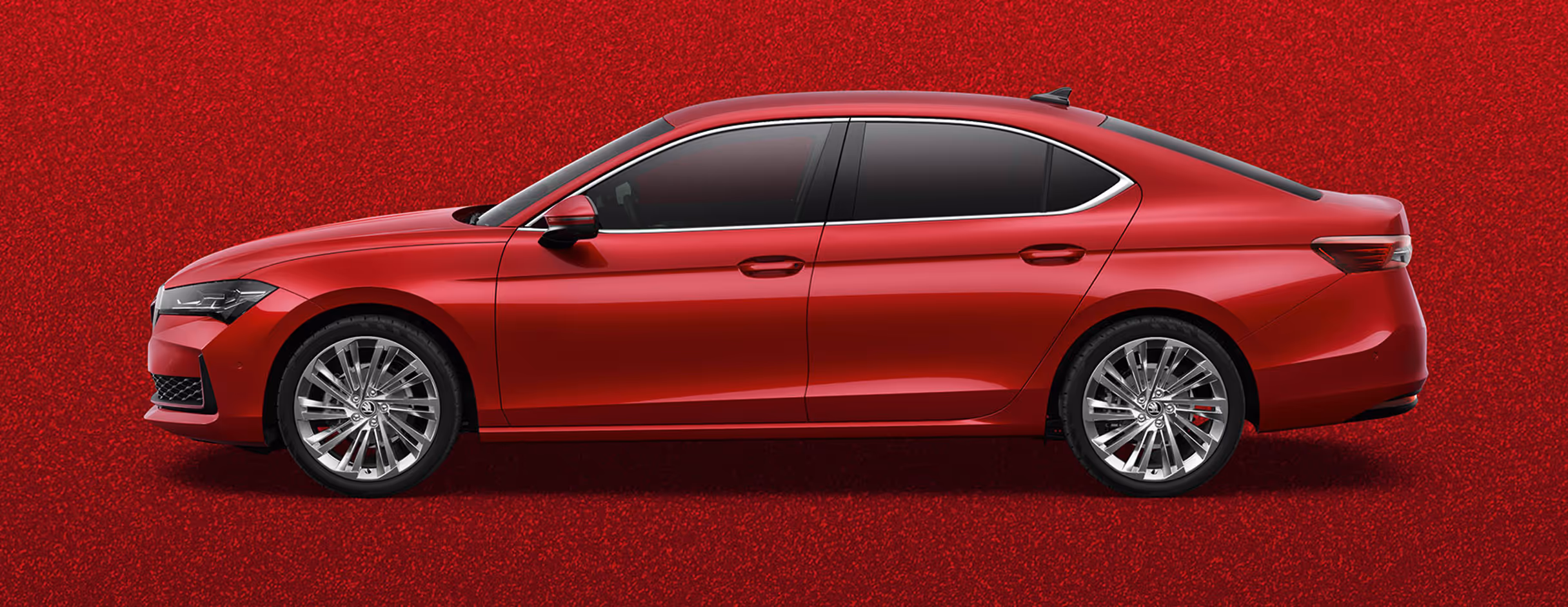 Seitenansicht einer Škoda Superb Limousine in der Lackierung Karmin-Rot Metallic mit 19 Zoll Leichtmetallfelgen “Veritate” vor einem einfarbigen Hintergrund in der Farbe der Fahrzeuglackierung.