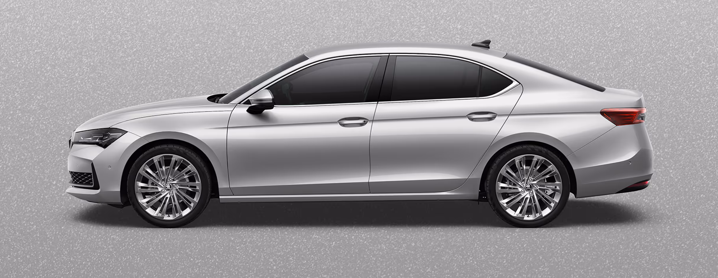 Seitenansicht einer Škoda Superb Limousine in der Lackierung Aluminium-Silber Metallic mit 19 Zoll Leichtmetallfelgen “Veritate” vor einem einfarbigen Hintergrund in der Farbe der Fahrzeuglackierung.