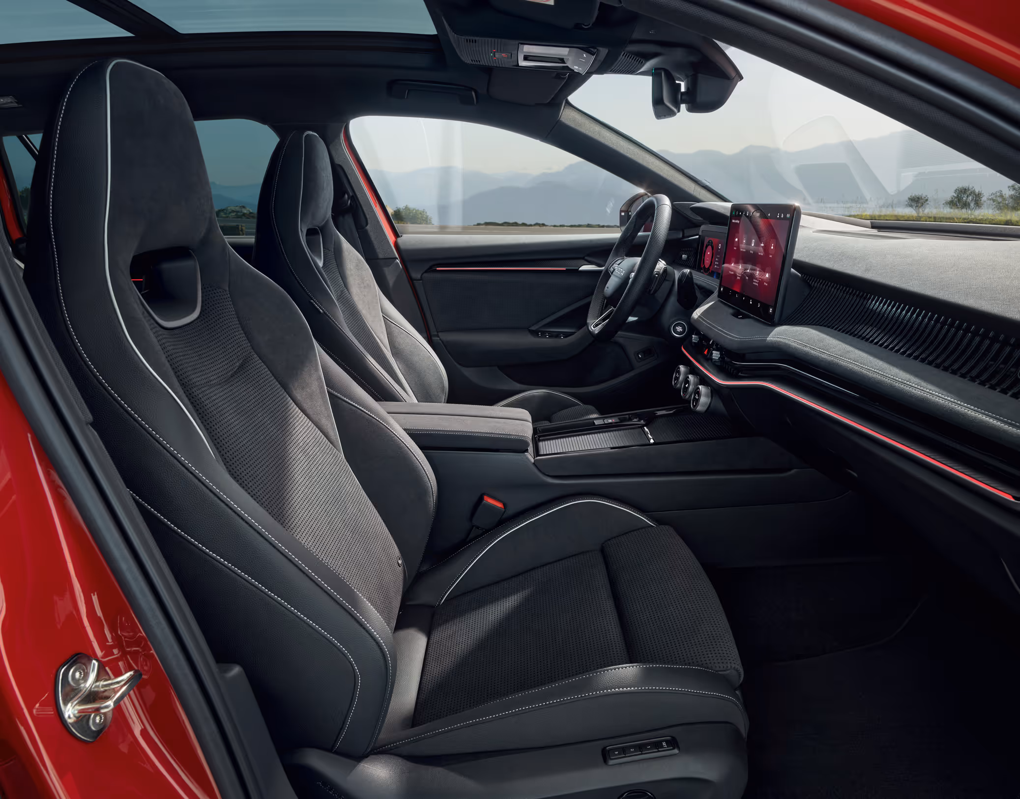 Eine seitliche Innenansicht des Škoda Superb zeigt das sportliche Interieur der Design Selection Sportline. Die schwarzen Sportsitze aus Dinamica Artvelour mit integrierten Kopfstützen sind mit schwarzem Venice-Kunstleder bezogen und werden durch graue Kontrastnähte akzentuiert. Durch die Fenster ist eine bergige Küstenlandschaft sichtbar.