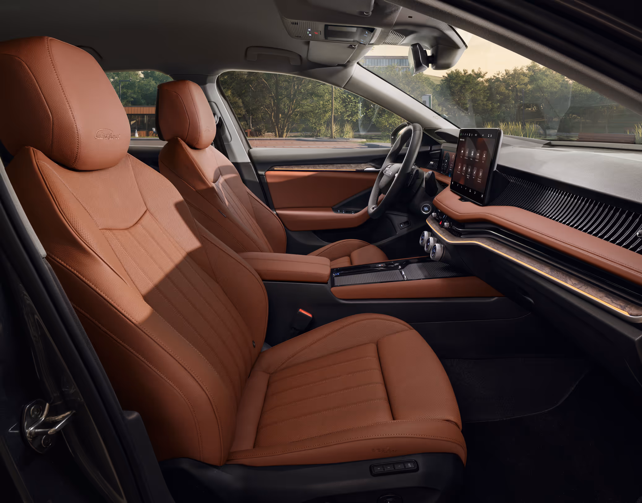 Eine seitliche Innenansicht des Škoda Superb zeigt das Interieur der Design Selection L&K Suite in Cognac. Die cognac-farbenen, perforierten Ledersitze mit „Laurin & Klement“-Schriftzug auf den Kopfstützen sowie das dunkle Armaturenbrett mit einer Dekorleiste in Unique Dark Chrome sind zu sehen, während durch die Fenster der Außenbereich eines modernen Gebäudes mit Bäumen sichtbar ist.