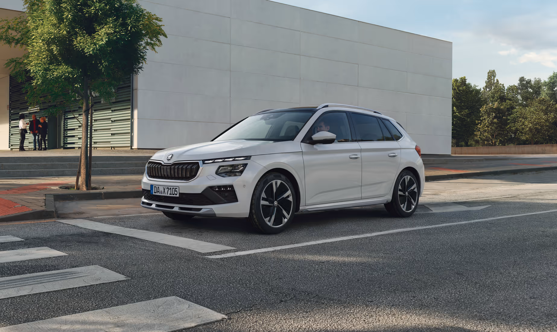 Ein Škoda Kamiq in der Ausstattungslinie Monte Carlo und der Lackierung Moon-Weiß Perleffekt hält an einem Zebrastreifen in einer städtischen Szenerie.