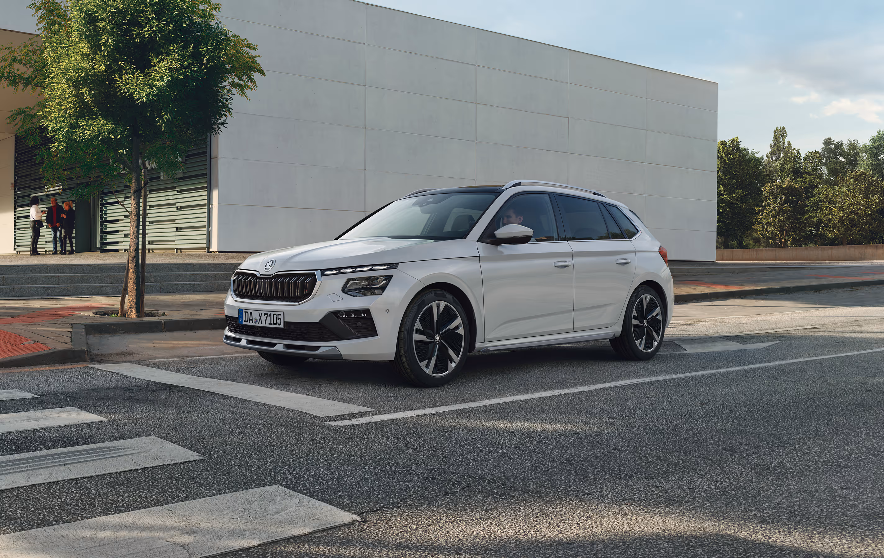 Ein Škoda Kamiq in der Ausstattungslinie Monte Carlo und der Lackierung Moon-Weiß Perleffekt hält an einem Zebrastreifen in einer städtischen Szenerie.