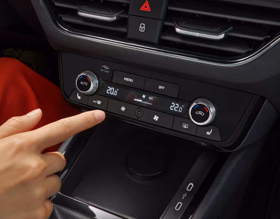 Eine Nahaufnahme zeigt das Bedienfeld der 2-Zonen-Klimaanlage Climatronic im Cockpit eines Škoda Kamiq. Ein Finger betätigt eine der Tasten unterhalb des zentralen Displays, auf dem die unterschiedlichen Temperatureinstellungen für Fahrer und Beifahrer angezeigt werden.