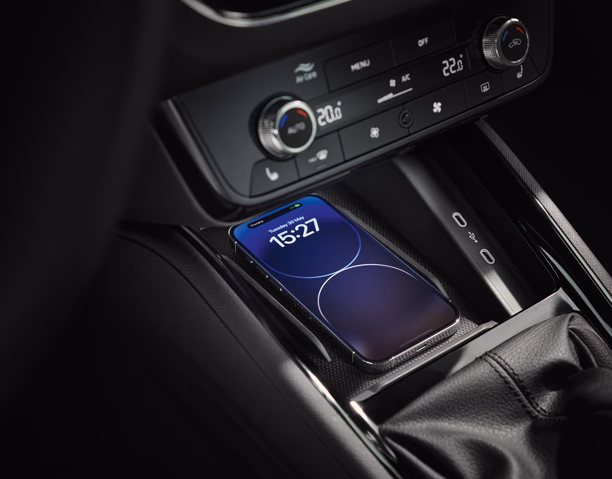 Eine Nahaufnahme zeigt die Phonebox in der Mittelkonsole eines Škoda Kamiq, in der ein Smartphone kabellos geladen wird. Auf dem Bildschirm des Telefons wird der Ladevorgang angezeigt. Neben der Ladeschale sind zwei USB-C-Anschlüsse zu sehen. Darüber das Bedienfeld der Klimaanlage.