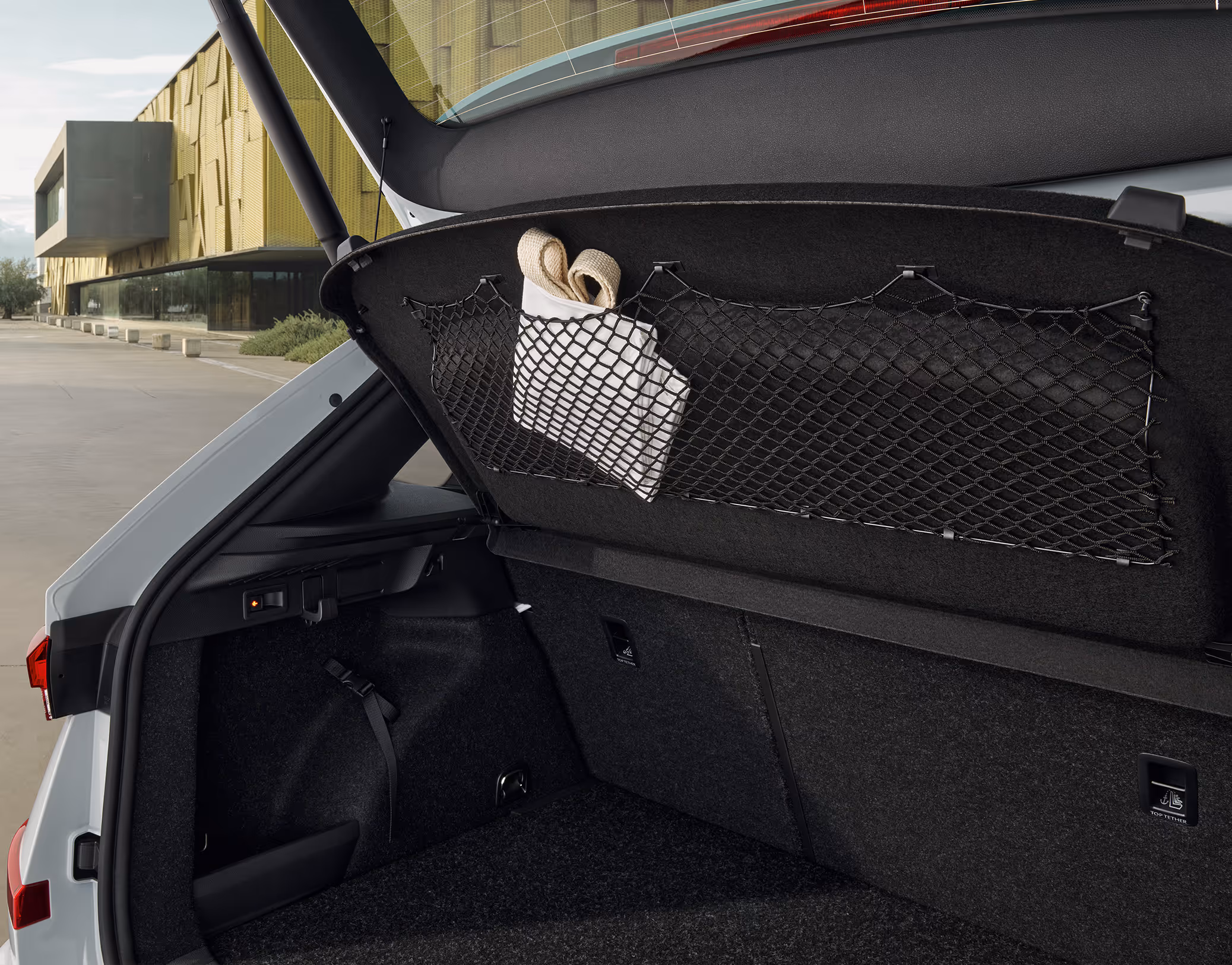 Eine Nahaufnahme zeigt die Unterseite der Gepäckraumabdeckung im Kofferraum eines Škoda Kamiq. An dieser Abdeckung ist ein schwarzes Gepäcknetz befestigt. Darin ist ein zusammengefalteter, heller Stoffbeutel verstaut.