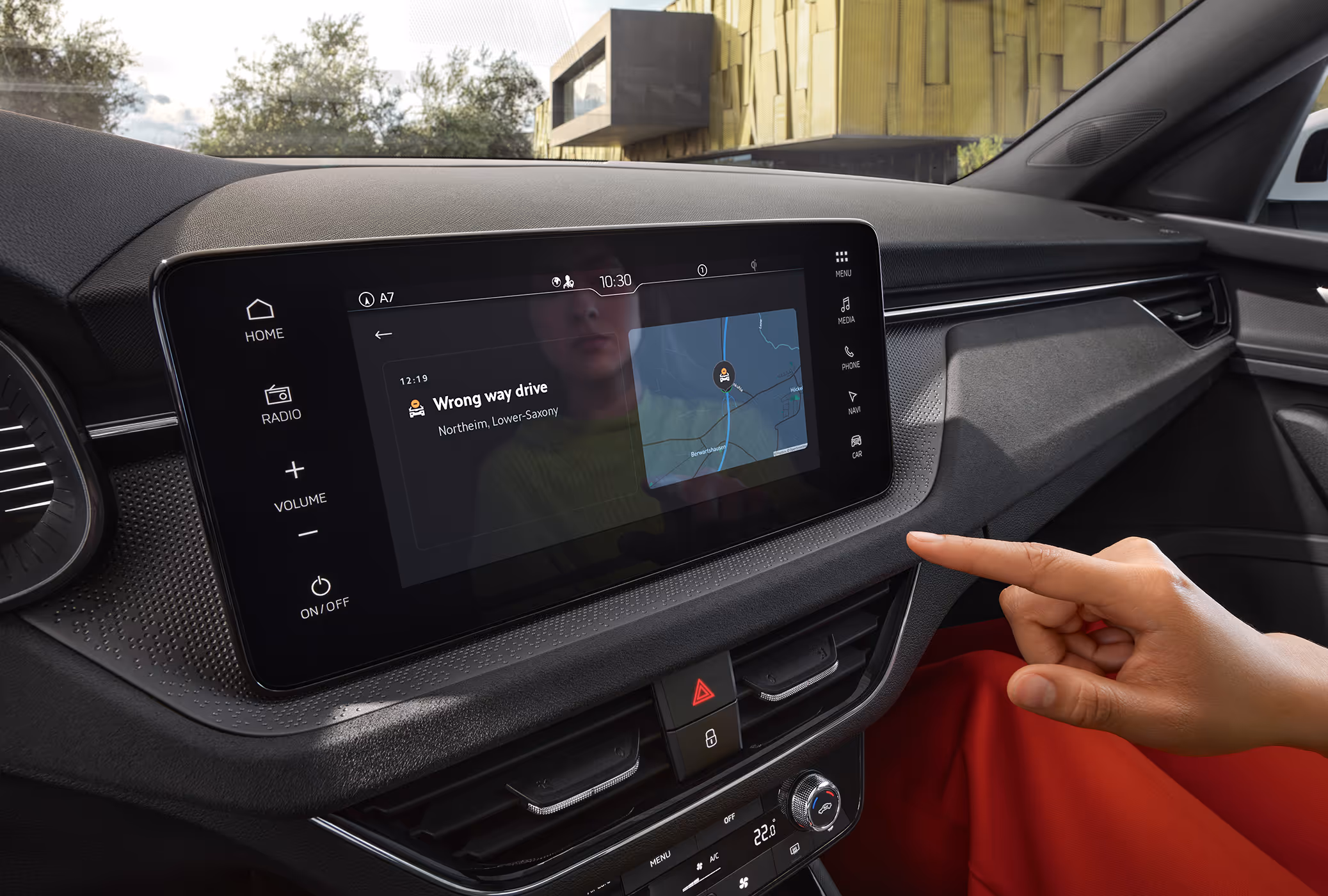 Eine Nahaufnahme zeigt das Infotainmentdisplay im Cockpit eines Škoda Kamiq, auf dem eine „Wrong way drive“-Warnung der Infotainment App Traffication angezeigt wird. Ein Finger deutet auf die Warnmeldung, die neben einer Kartendarstellung der aktuellen Position erscheint.