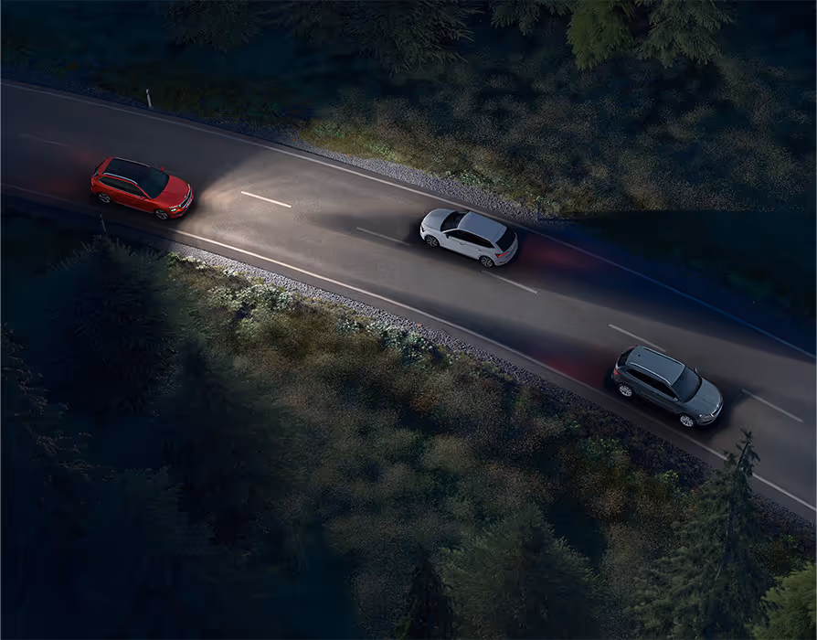 Animation des Dynamischen Fernlichtassistenten: Ein roter Škoda Kamiq fährt nachts auf einer Landstraße und leuchtet die Fahrbahn mit Fernlicht aus. Das System erkennt entgegenkommende und vorausfahrende Fahrzeuge und blendet diese gezielt aus dem Lichtkegel aus, um eine Blendung zu vermeiden..