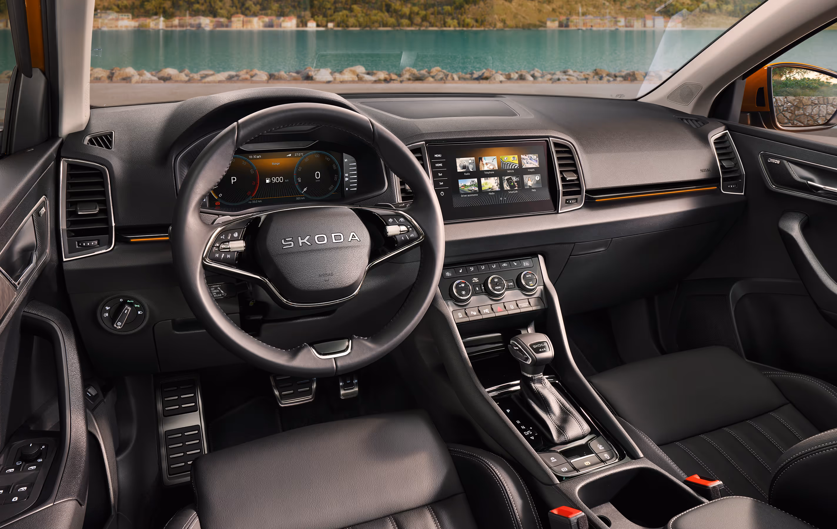 Eine Innenansicht des Škoda Karoq zeigt das Cockpit mit Blick auf eine Küstenlandschaft. Das schwarze Interieur ist mit einem Multifunktionslenkrad, einem digitalen Cockpit und einem zentralen Infotainmentbildschirm ausgestattet. Details wie die Pedalerie in Edelstahloptik und orangefarbene Akzente am Armaturenbrett sind sichtbar. Unten rechts steht auf einer dunkelgrün abgesetzten Fläche "Smarte Details" geschrieben.