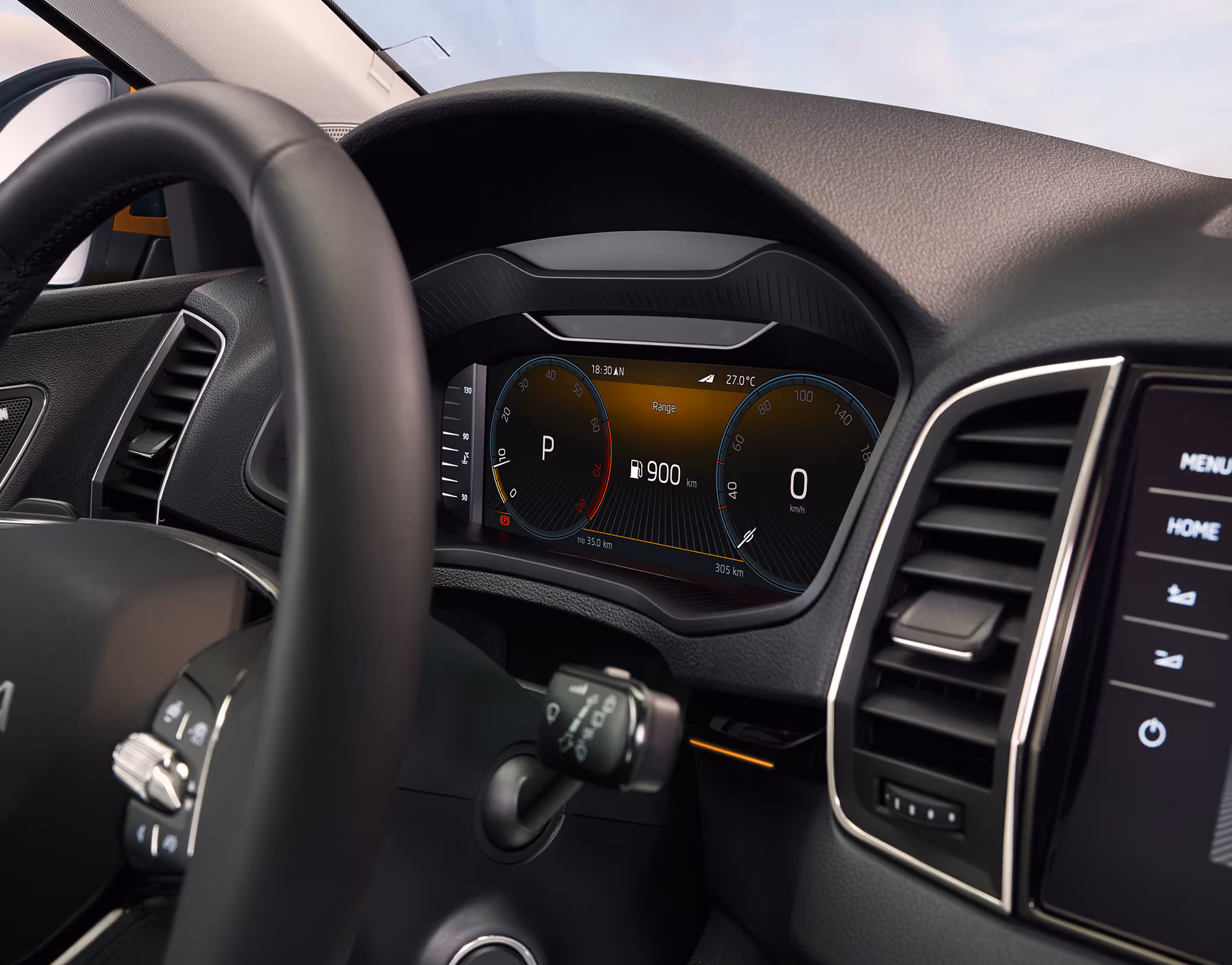 Eine Nahaufnahme des Digitalen Cockpits in einem Škoda Karoq zeigt die klassische Ansicht mit zwei virtuellen Rundinstrumenten. Das Display zeigt eine Reichweite von 900 km, die Fahrstufe "P" und eine Geschwindigkeit von 0 km/h an. In der Aufnahme sind auch ein Teil des Lenkrads, der Start-Stopp-Knopf und der rechte Lüftungsschacht zu sehen.
