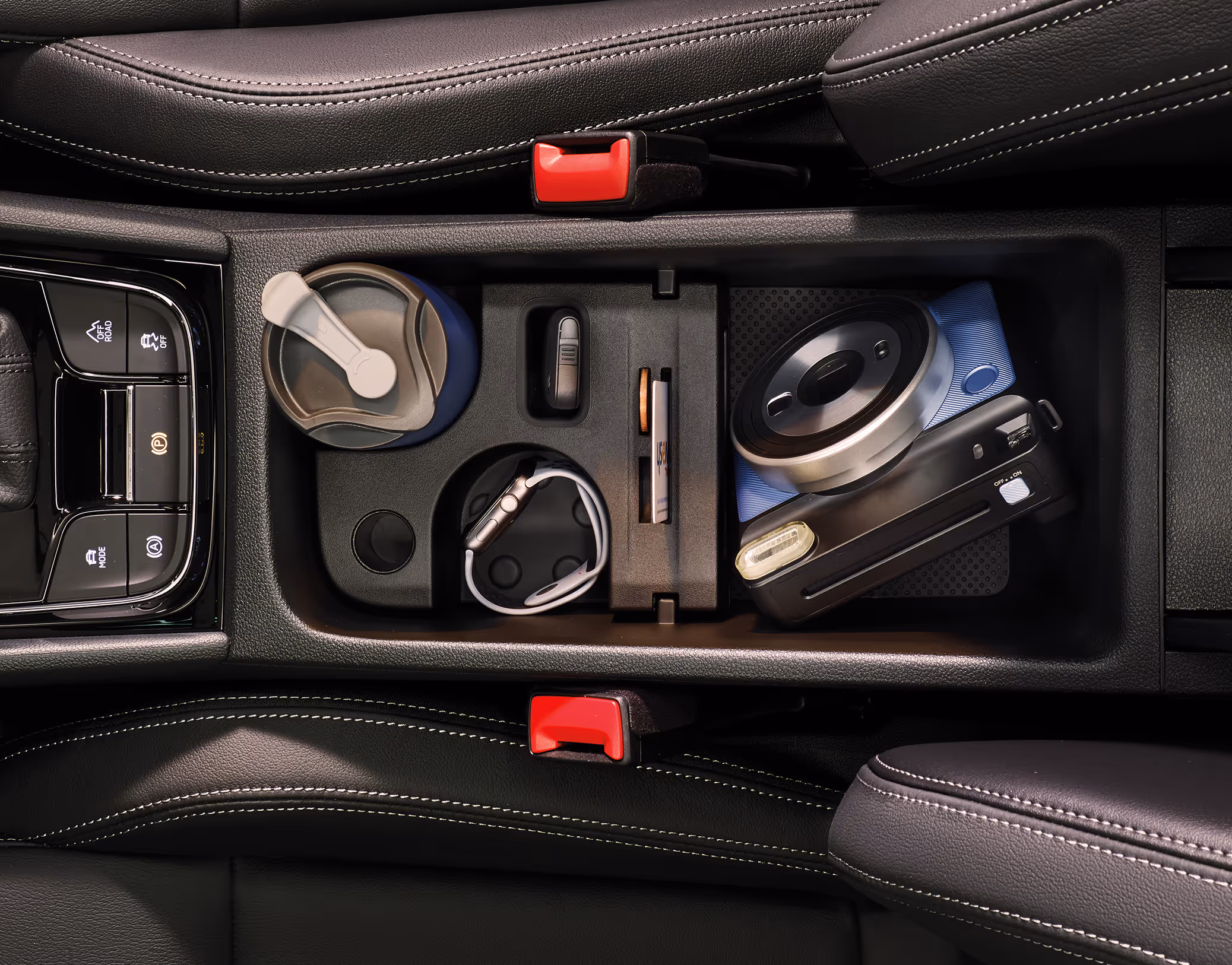 Eine Draufsicht zeigt die geöffnete Jumbo Box in der Mittelkonsole eines Škoda Karoq, die sich zwischen den beiden Vordersitzen befindet. Die verschiedenen Fächer und Halterungen sind mit Alltagsgegenständen wie einem Thermobecher, einem Autoschlüssel, einem Stift und einer Kompaktkamera gefüllt.