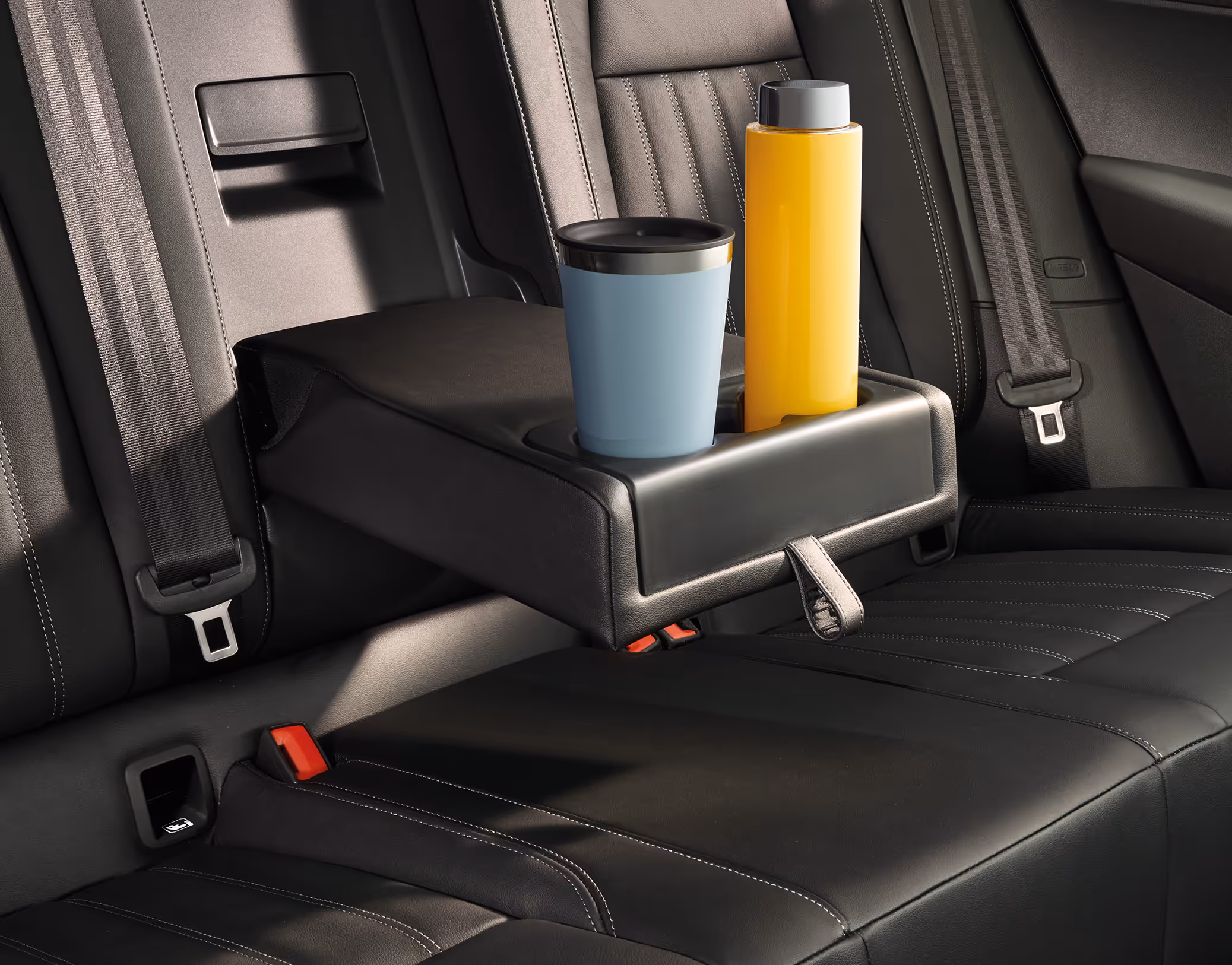 Eine Nahaufnahme der Rücksitzbank eines Škoda Karoq zeigt die heruntergeklappte Mittelarmlehne. In den integrierten Getränkehaltern stehen ein hellblauer Thermobecher und eine gelbe Trinkflasche, umgeben von der schwarzen Lederausstattung.
