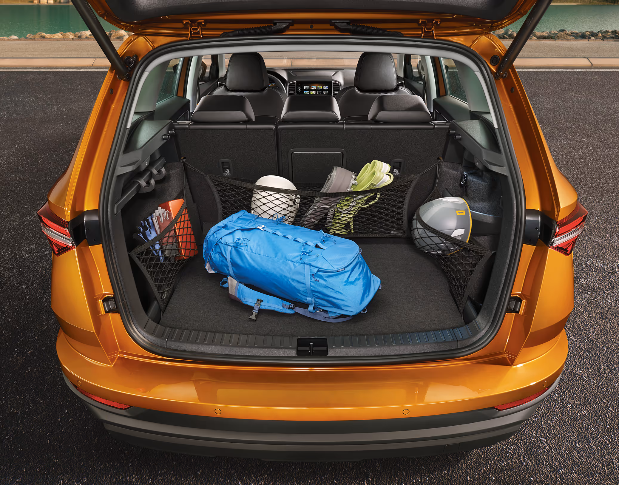 Eine Ansicht des geöffneten Kofferraums eines Škoda Karoq zeigt die Anwendung des Netzsystems. Ein blauer Rucksack liegt auf dem Kofferraumboden, während verschiedene Gepäcknetze an den Seiten und an der Rücksitzlehne weitere Gegenstände wie einen Helm, Schuhe und Handschuhe sichern.