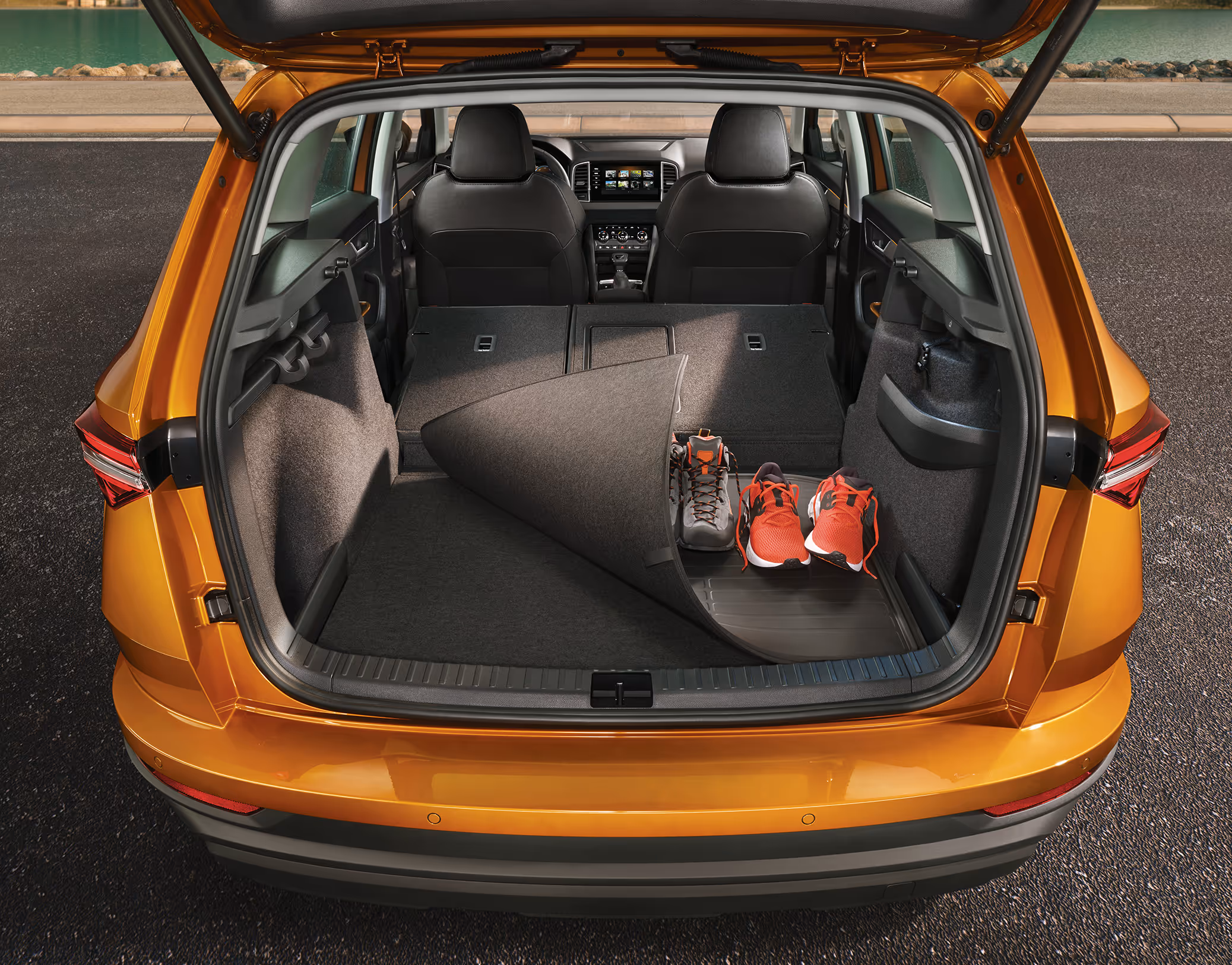 Eine Ansicht des geöffneten Kofferraums eines Škoda Karoq zeigt die Wendematte für den Kofferraumboden. Die Matte ist teilweise umgeschlagen, um die abwaschbare Gummiseite zu zeigen, auf der ein Paar Wanderschuhe und ein Paar Turnschuhe stehen, während die andere Seite aus Teppich besteht.