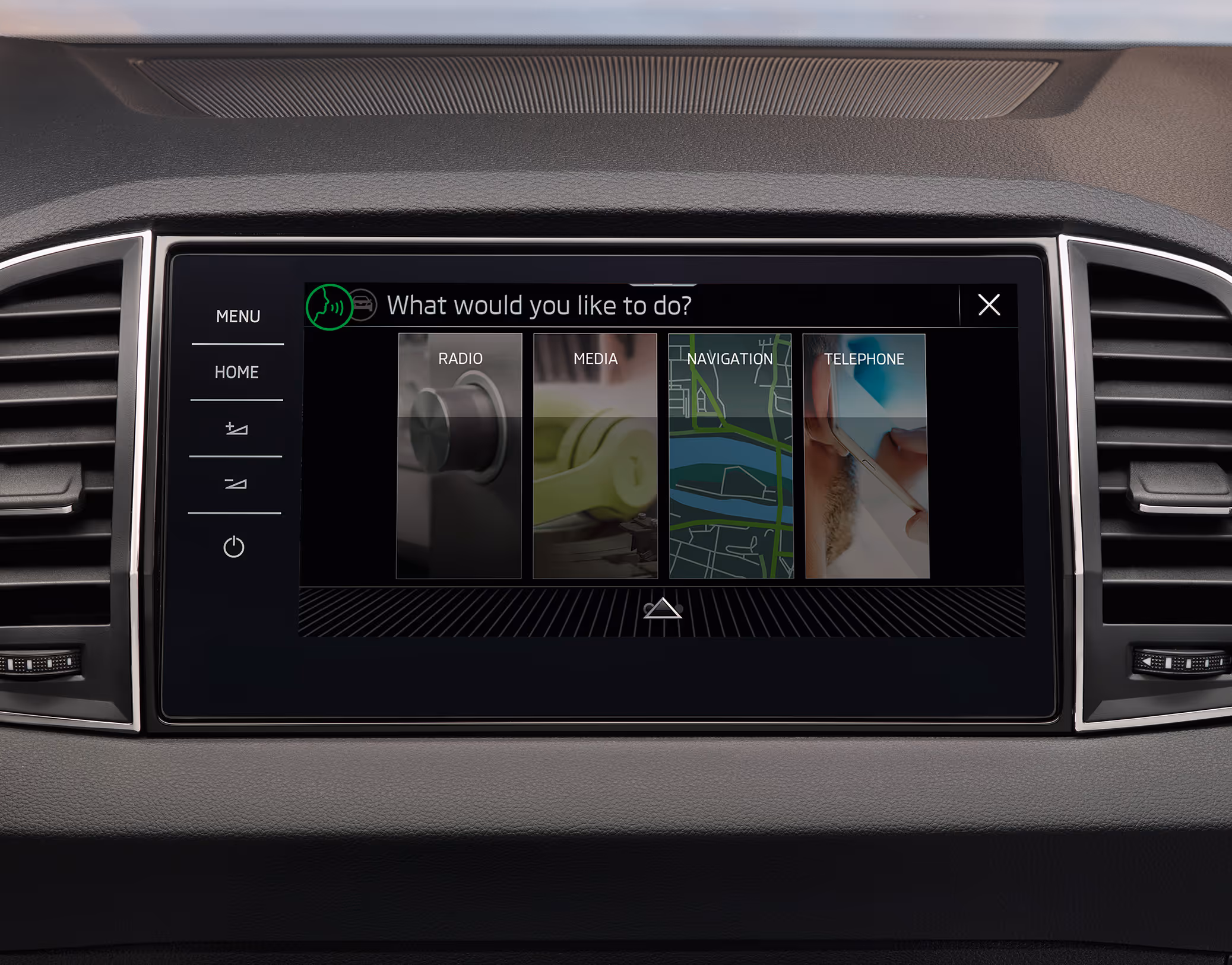 Eine Nahaufnahme des Infotainmentsystems im Cockpit eines Škoda Karoq zeigt die aktive Sprachsteuerungs-Oberfläche. Auf dem Display erscheint die Frage „What would you like to do?“ über Auswahlkacheln für die Funktionen Radio, Media, Navigation und Telefon.