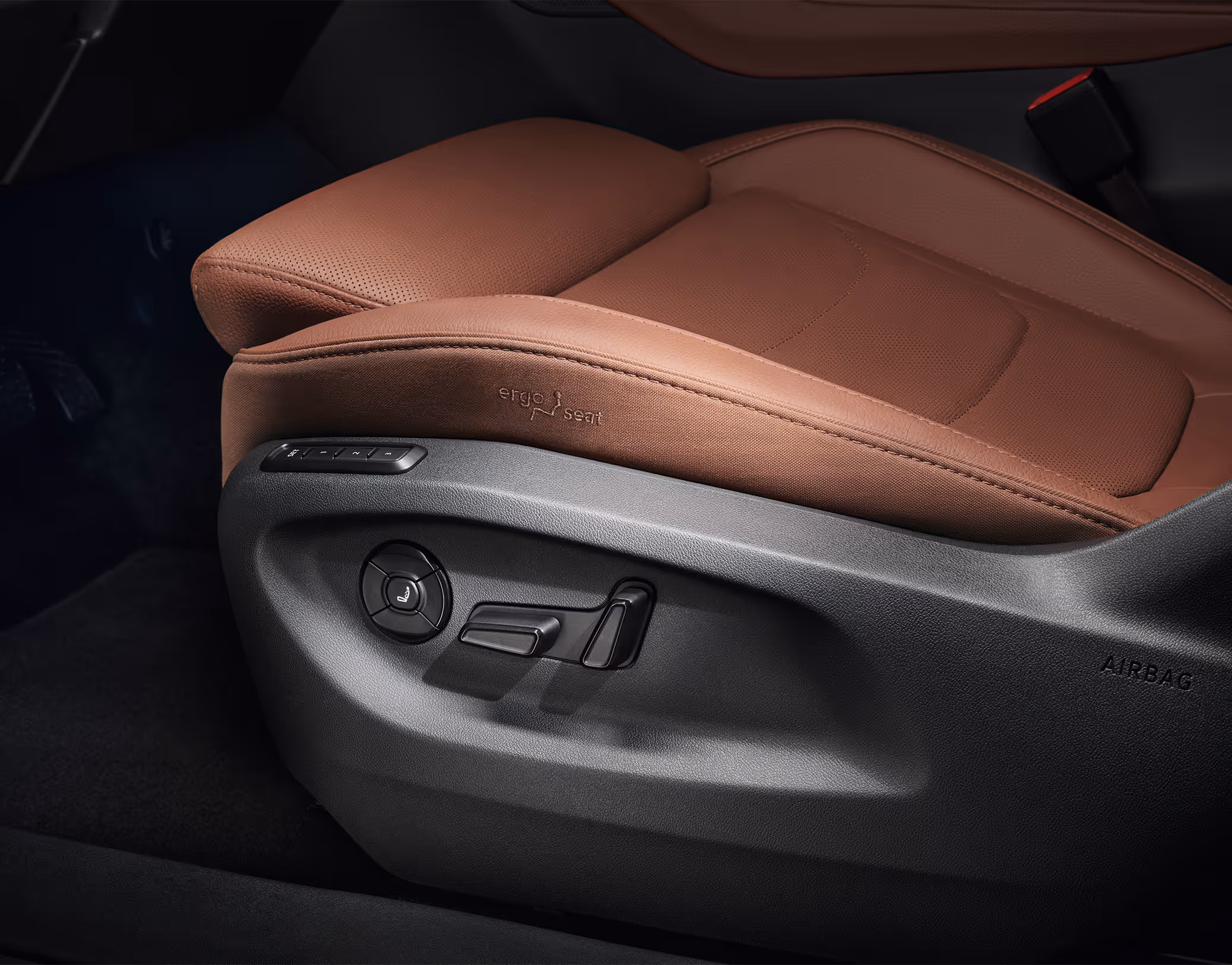 Eine Nahaufnahme zeigt den Ergo-Sitz eines Škoda Kodiaq, der mit cognac-braunem Leder der Design Selection Lounge bezogen ist. An der Seite des Sitzes sind die Bedienelemente für die elektrische Verstellung und die pneumatische Massagefunktion deutlich zu erkennen. Diese Schalter ermöglichen eine präzise Anpassung der Sitzposition für den Fahrer oder Beifahrer.