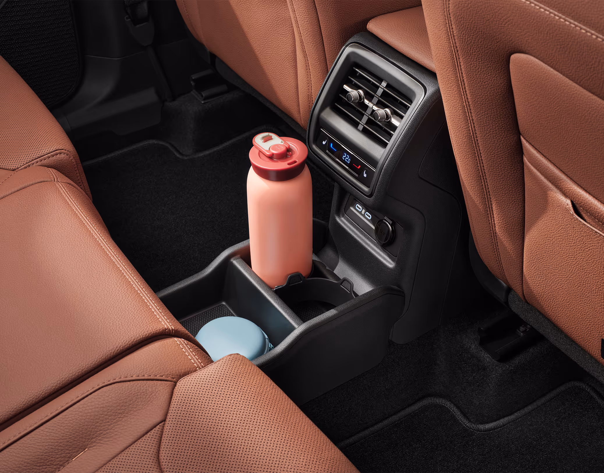 Eine Nahaufnahme zeigt den hinteren Teil der Mittelkonsole im Škoda Kodiaq. Unter den Lüftungsdüsen und den Bedienelementen für die 3-Zonen-Klimaanlage befinden sich zwei USB-C-Anschlüsse und ein großes Ablagefach mit Getränkehalter. Die cognac-braunen Ledersitze der Design Selection Lounge rahmen die Szene ein.