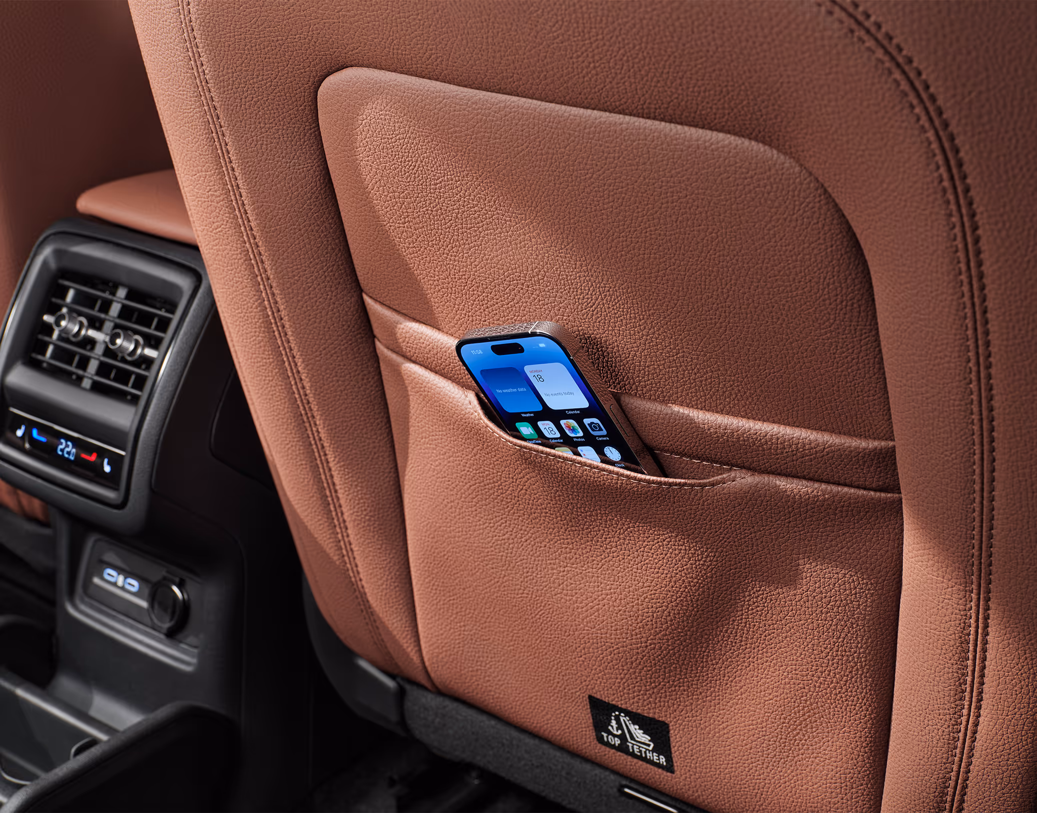 Eine Nahaufnahme zeigt eine der Smartphone-Taschen an der Rückseite eines Vordersitzes im Škoda Kodiaq. Ein Smartphone steckt sicher in der dafür vorgesehenen Tasche, die in den cognac-braunen Lederbezug der Design Selection Lounge integriert ist.