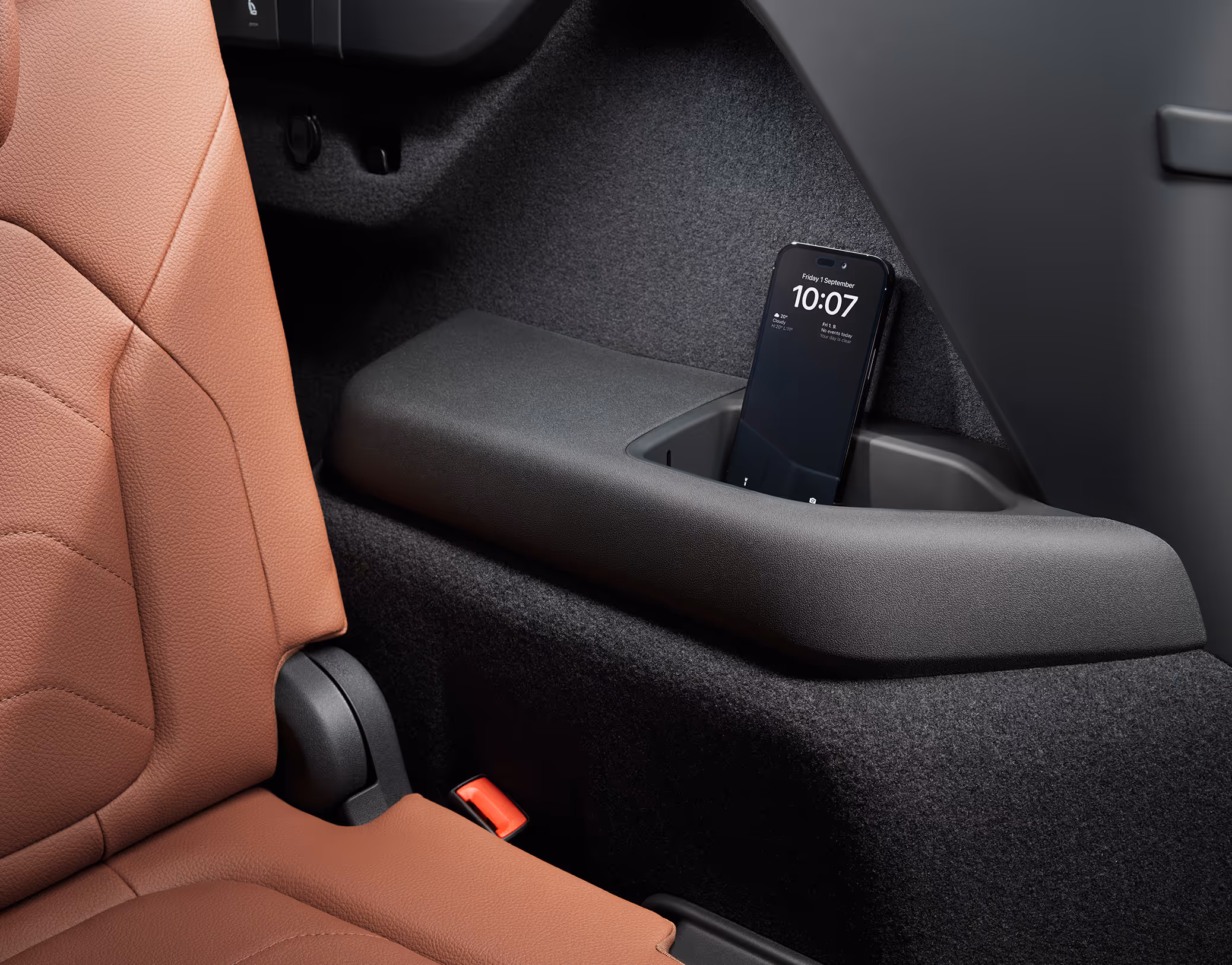 Eine Nahaufnahme zeigt eine der Smartphone-Taschen, die sich an der Rückseite der Mittelkonsole eines Škoda Kodiaq befindet. Ein Smartphone steckt sicher in der dafür vorgesehenen Halterung. Links im Bild ist ein Teil des Sitzes mit cognac-braunem Lederbezug der Design Selection Lounge zu sehen.