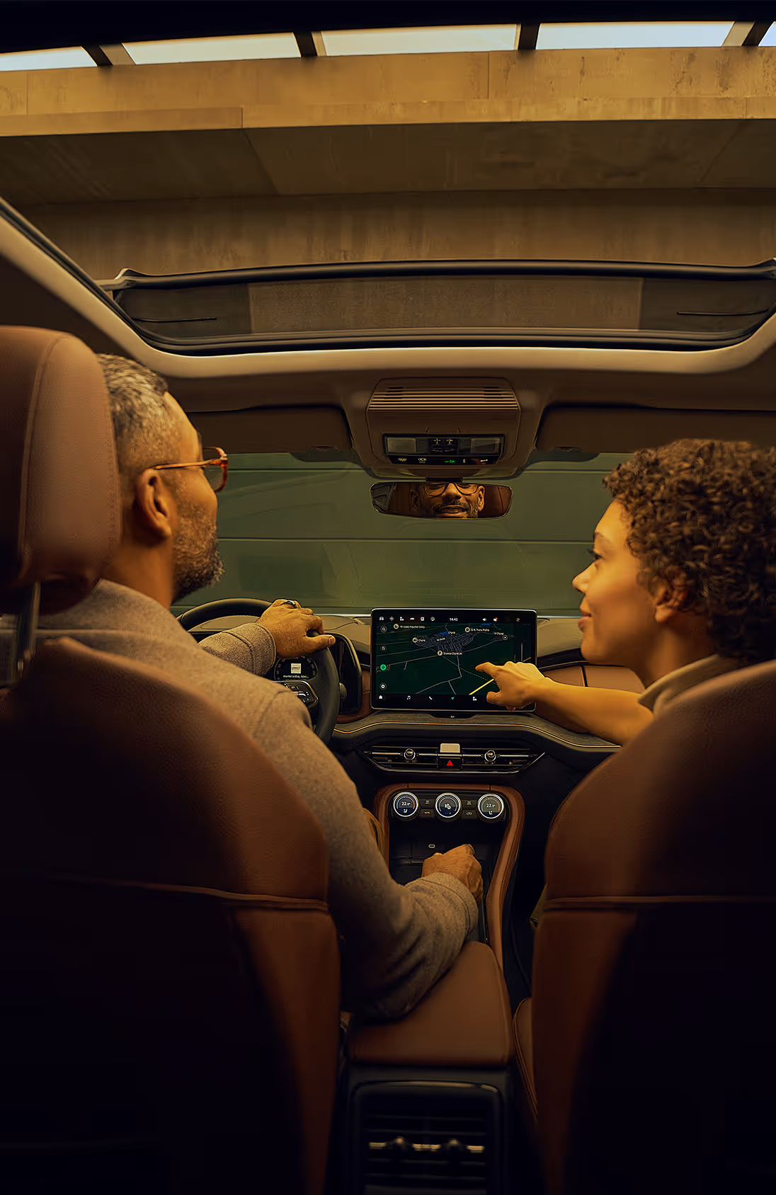 Blick von der Rückbank aus auf ein Paar im vorderen Teil eines Škoda Kodiaq. Die Beifahrerin interagiert mit dem großen Infotainmentdisplay und zeigt auf die Navigationskarte, während der Fahrer ebenfalls dorthin schaut. Das Interieur mit den cognac-braunen Ledersitzen der Design Selection Lounge ist stimmungsvoll beleuchtet.  Unten rechts steht auf einer dunkelgrün abgesetzten Fläche geschrieben: "Škoda Connect"