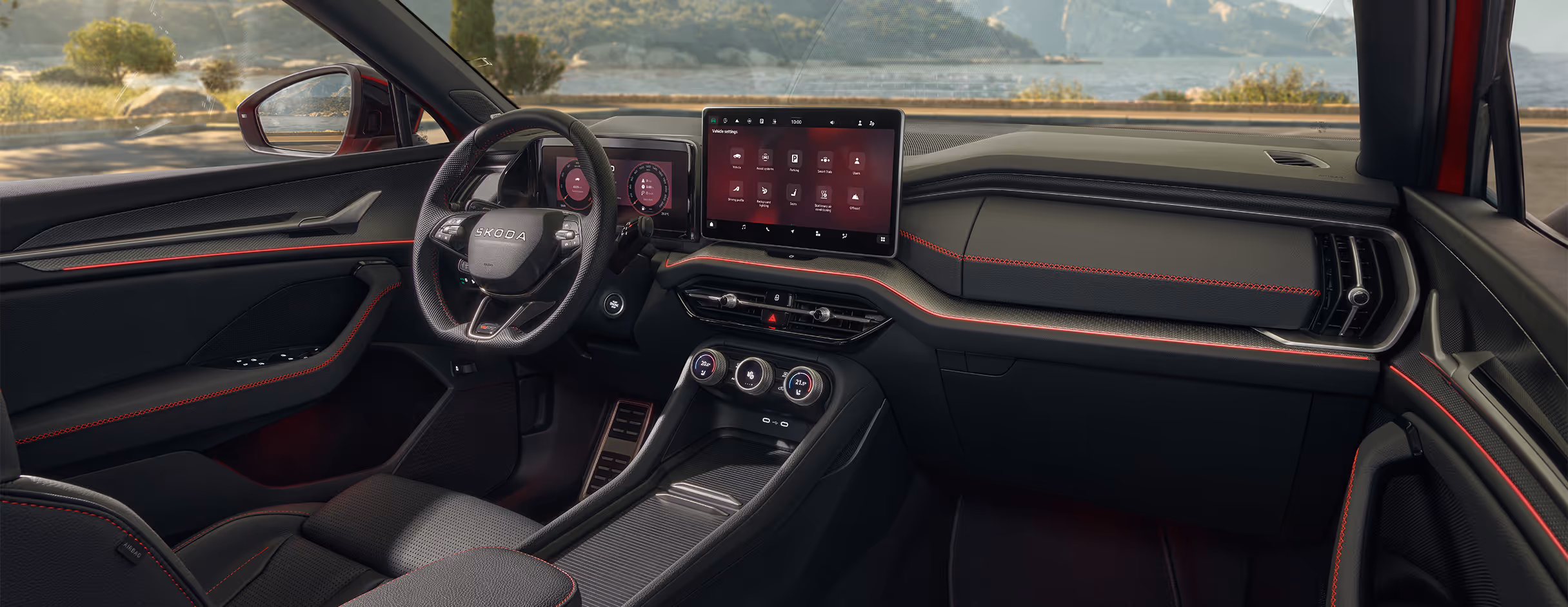 Eine weite Innenansicht zeigt das Cockpit des Škoda Kodiaq RS mit der Design Selection RS Lounge. Das sportliche Ambiente wird durch schwarze Sportsitze mit roten Kontrastnähten sowie roten Akzenten am Armaturenbrett und den Türverkleidungen geprägt. Durch die großen Fensterflächen eröffnet sich ein weiter Blick auf eine Küsten- und Berglandschaft.