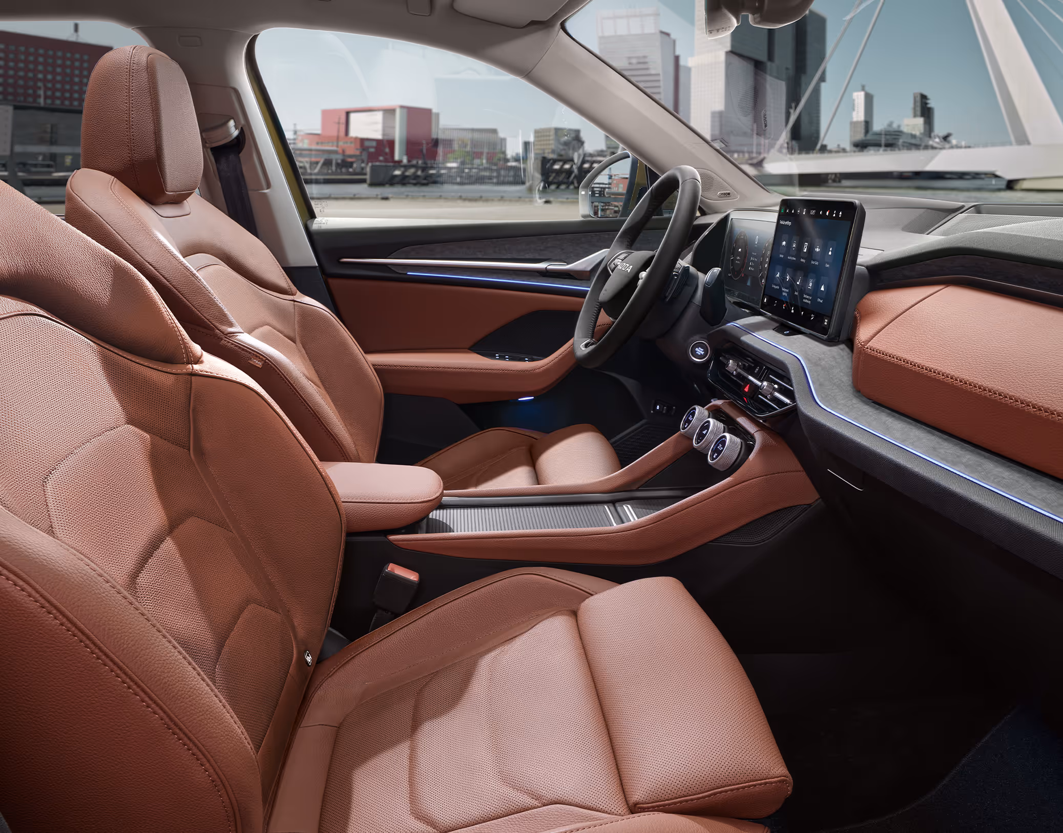 Eine seitliche Innenansicht des Škoda Kodiaq zeigt das Interieur der Design Selection Suite in Cognac. Die cognac-braunen, perforierten Ledersitze sowie das dunkle Armaturenbrett mit einer Dekorleiste in Unique Dark Brushed sind zu sehen, während durch die Fenster eine helle, städtische Szenerie sichtbar ist.